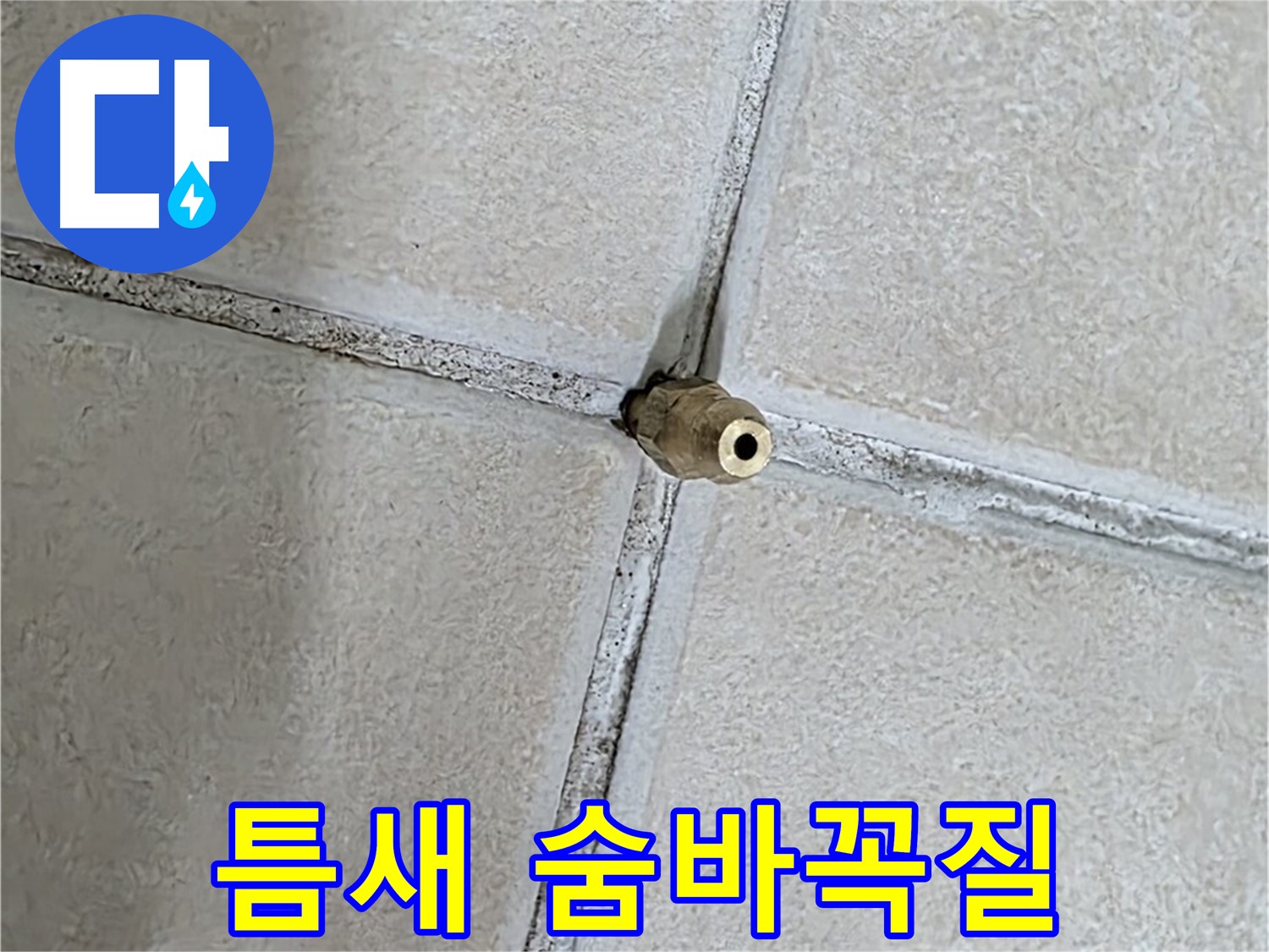 베이지색 타일 바닥에 위치한 금속 재질의 배관 연결 소켓 부분