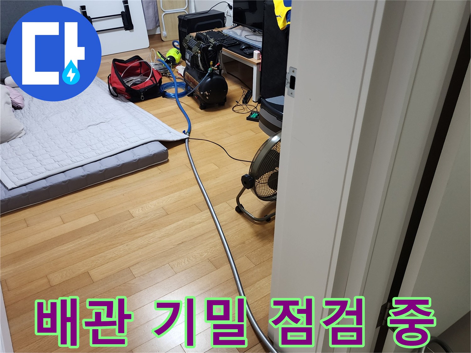 아파트 거실 바닥에 놓여 있는 누수 탐지용 콤프레샤와 파란색 호스