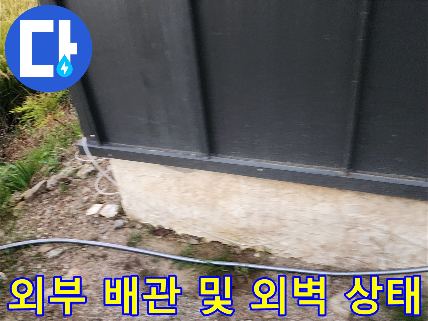 외벽 판넬 하단부의 젖은 콘크리트와 노출된 배관 라인