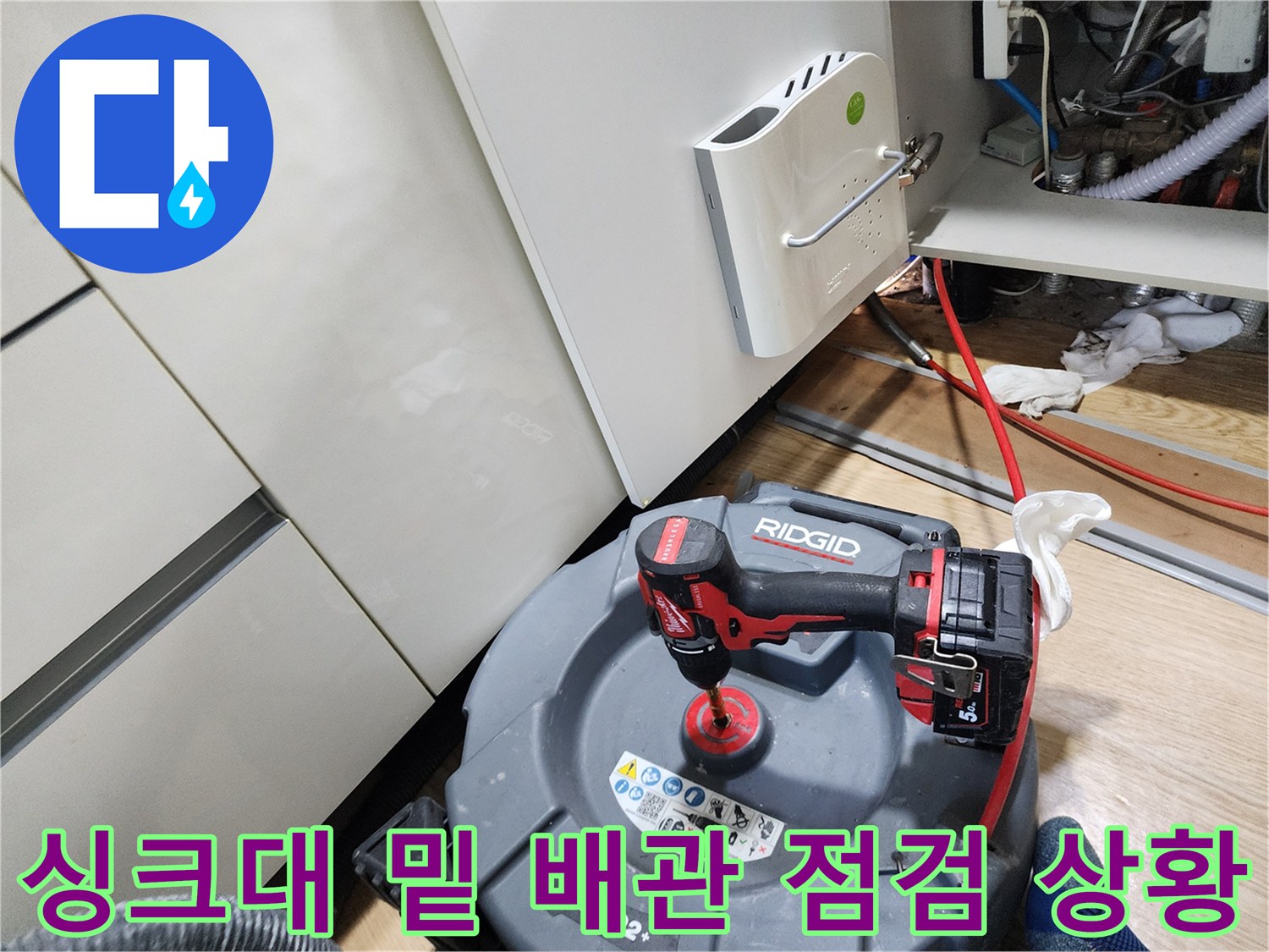 주방 가구 하단 좁은 공간에 배치된 배관 탐지 장비와 작업 도구들입니다.