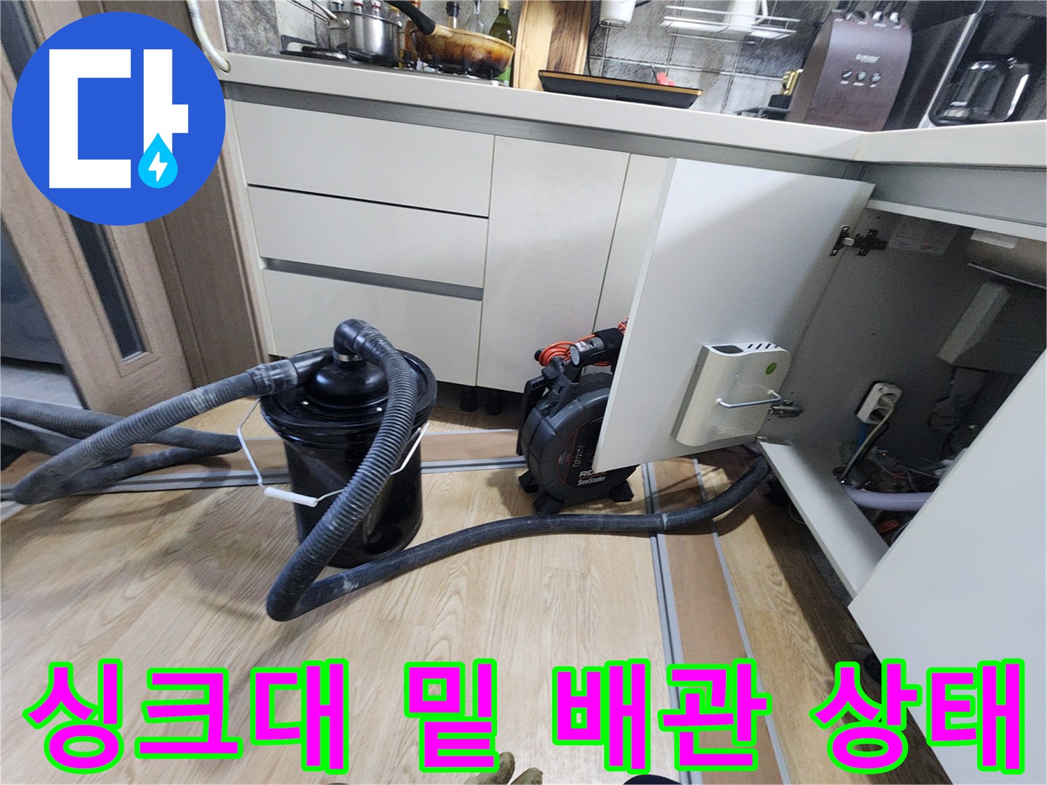 주방 싱크대 하단부에 배치된 배관 점검 장비와 호스입니다.