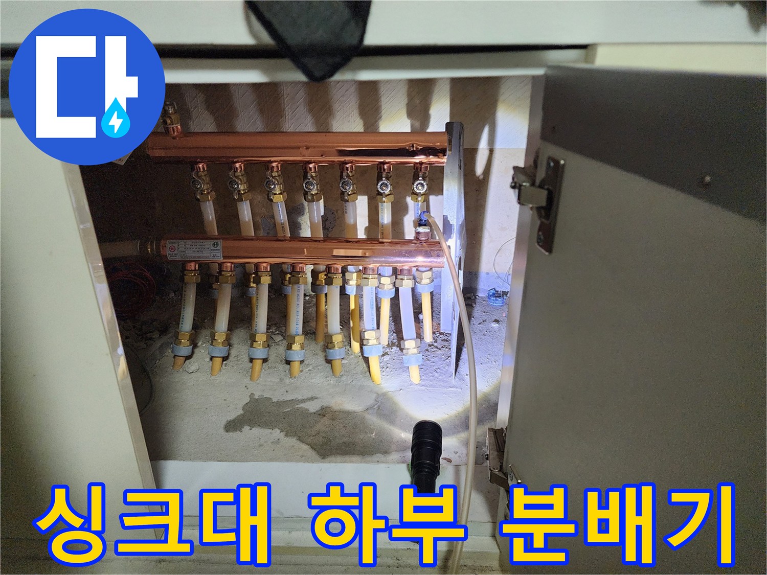 싱크대 하단에 위치한 난방 분배기와 여러 갈래의 배관들을 보여줍니다.