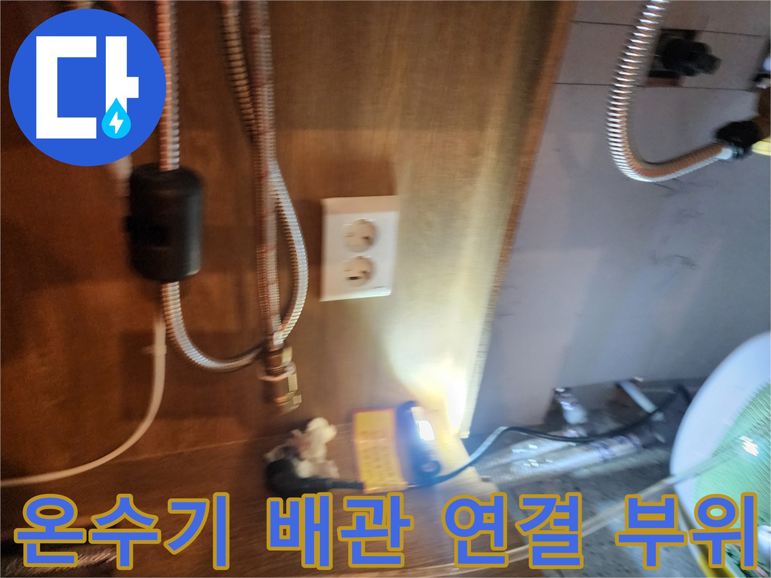 주방 싱크대 하단 전기 온수기와 금속 호스 연결 모습