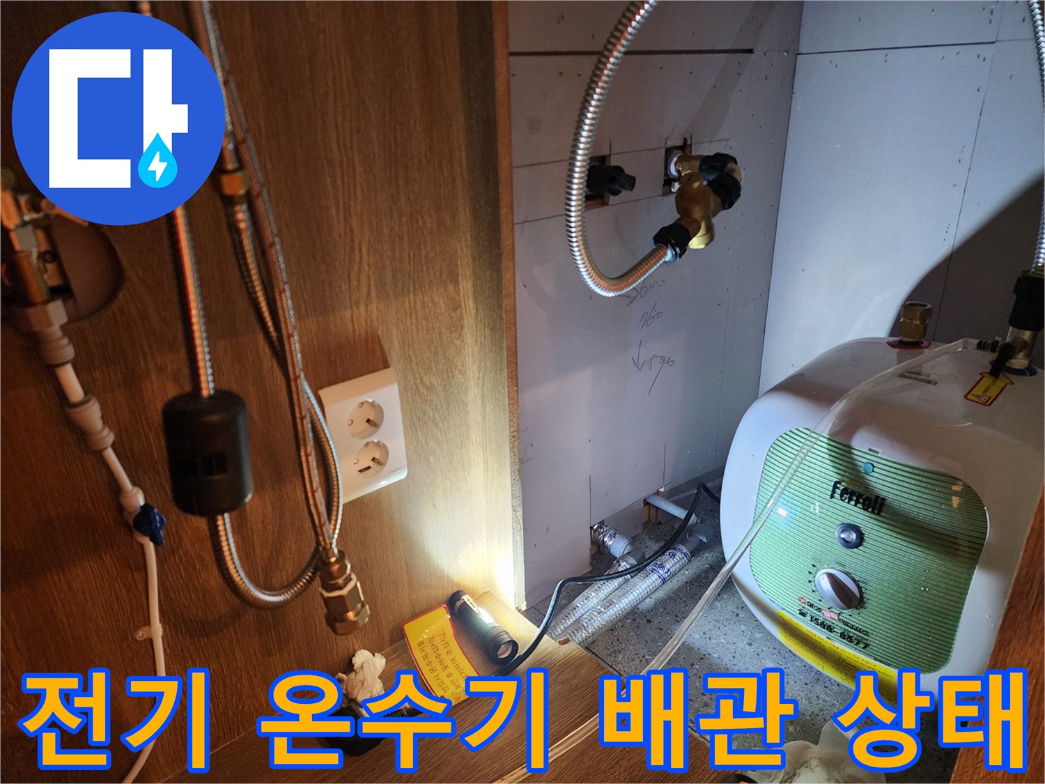 주방 하부장 내 설치된 전기 온수기와 연결된 금속 배관 모습