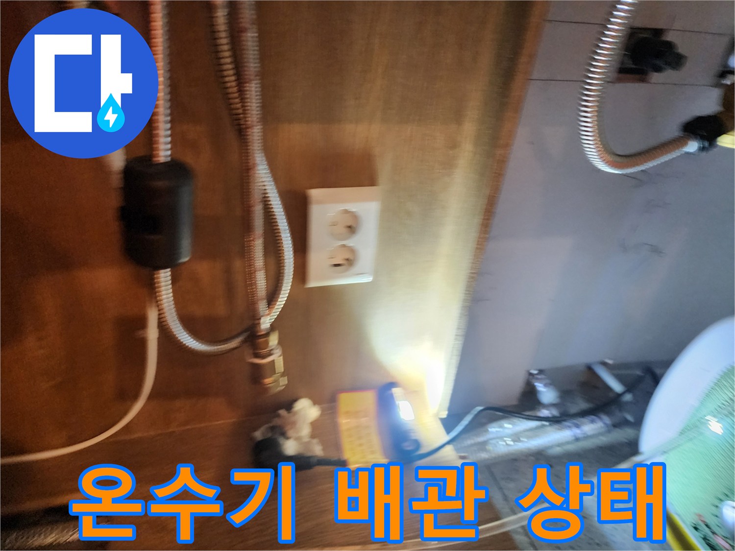 주방 하부장 내 설치된 전기 온수기와 연결된 금속 호스 모습