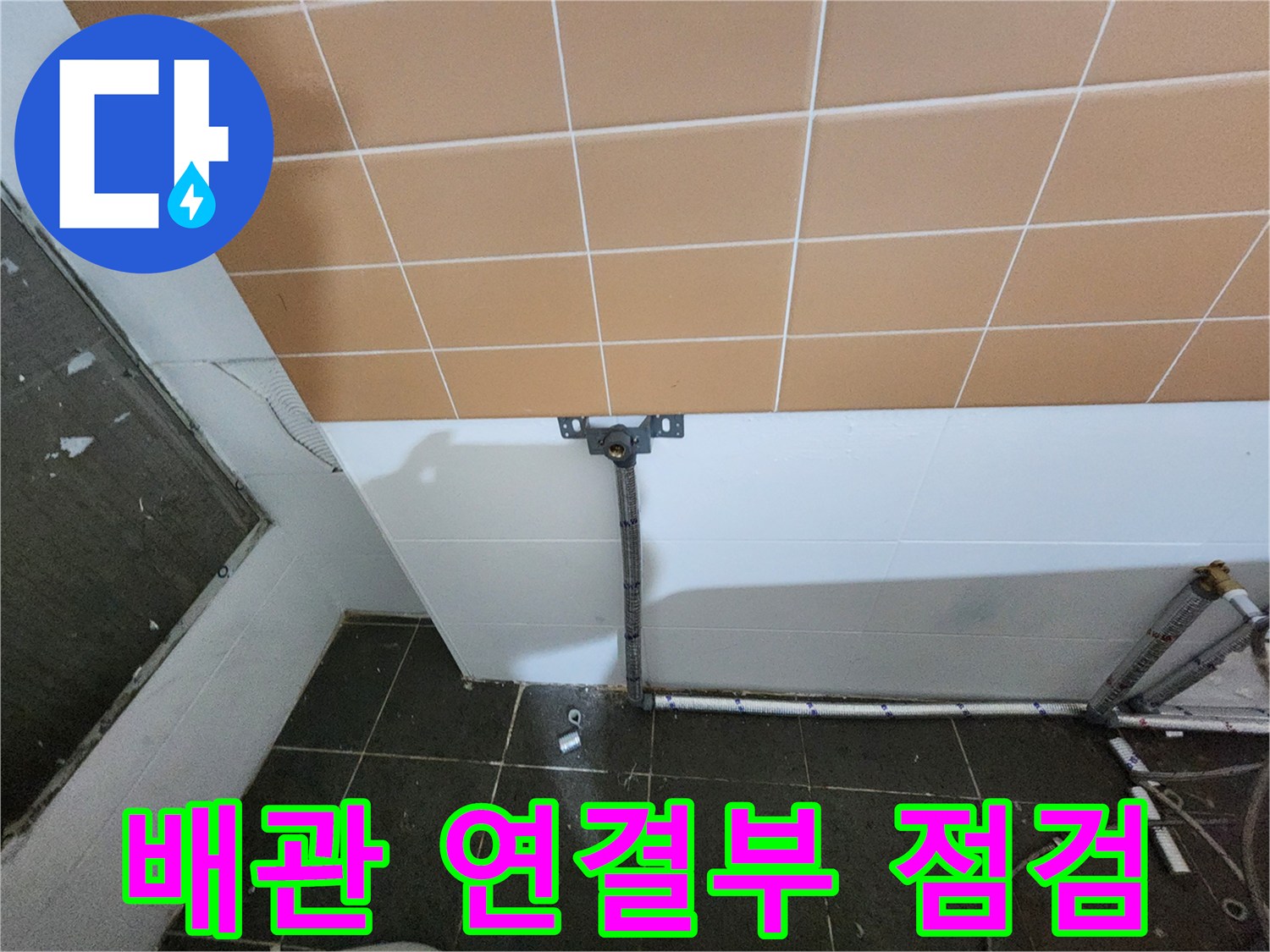 타일 벽면 아래로 노출된 배관과 지지대 상세 사진입니다.