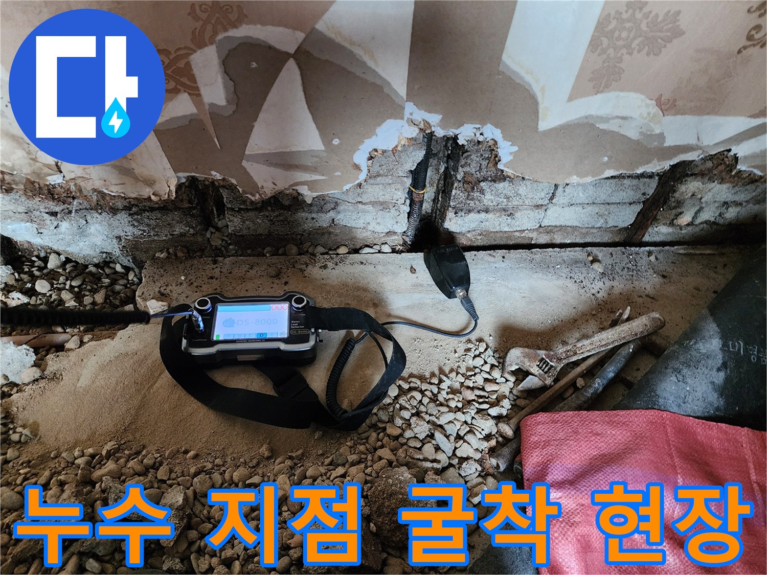 벽면 하단 배관의 물샘을 찾기 위해 벽지를 제거하고 탐지기를 사용하는 장면입니다.