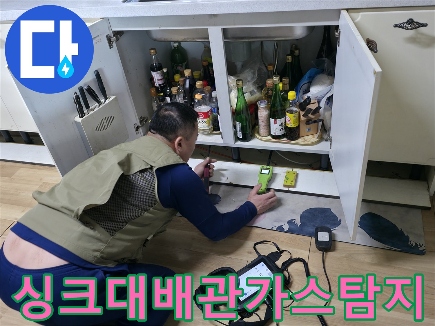 엔지니어가 싱크대 하부장 아래에서 가스 탐지기로 누수를 추적하고 있습니다.