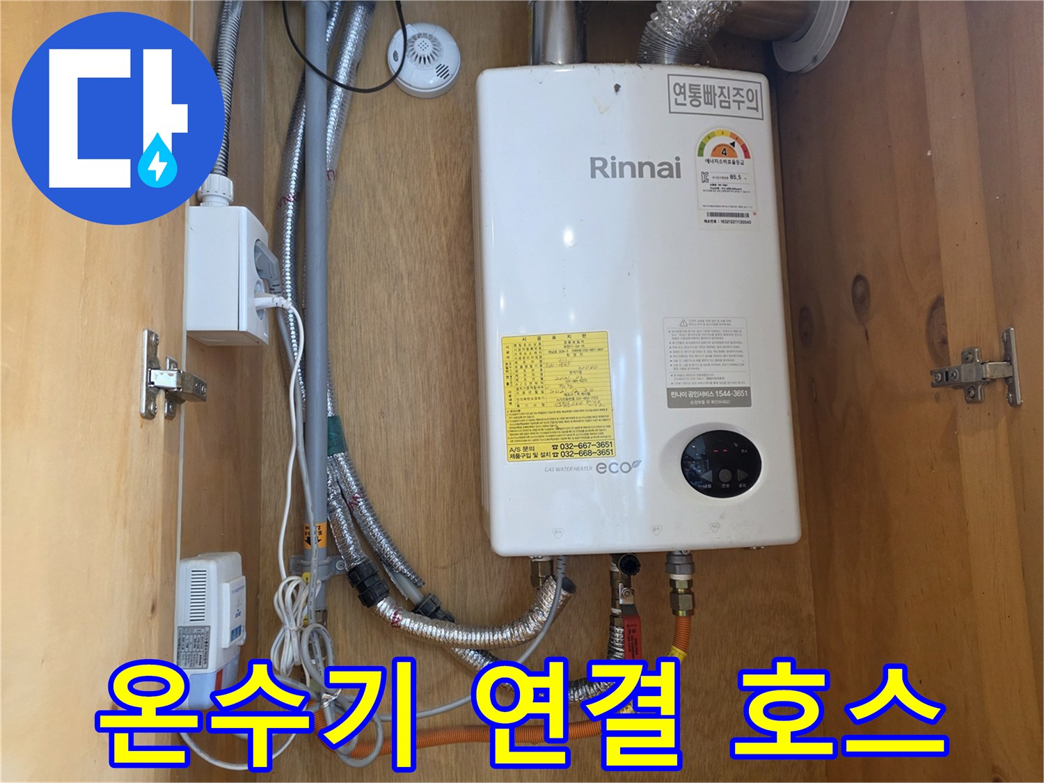 가스 온수기 하단의 금속 배관 및 주황색 호스 연결부