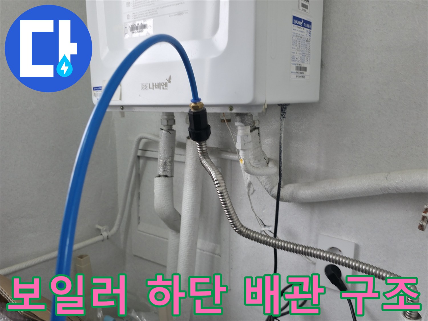하얀색 보일러 아래로 연결된 은색 굴곡 배관과 파란색 호스 상세 사진