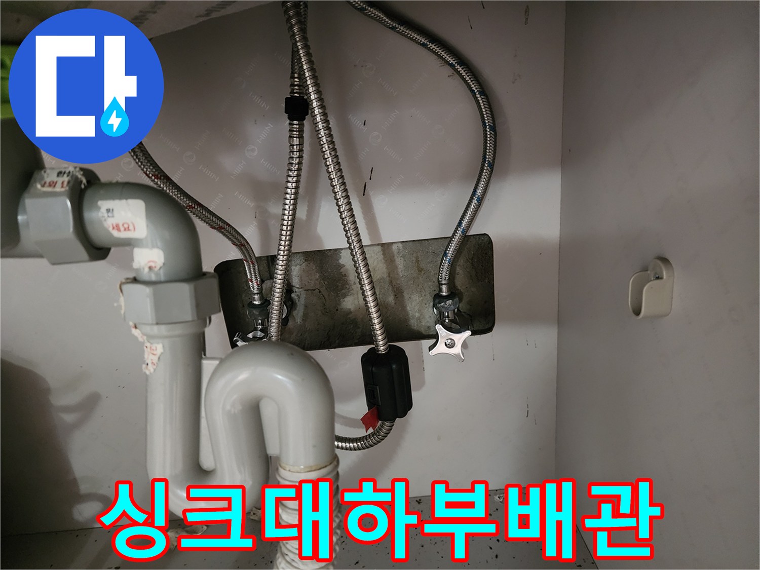금속 주름관과 하얀색 배수 호스가 연결된 싱크대 내부