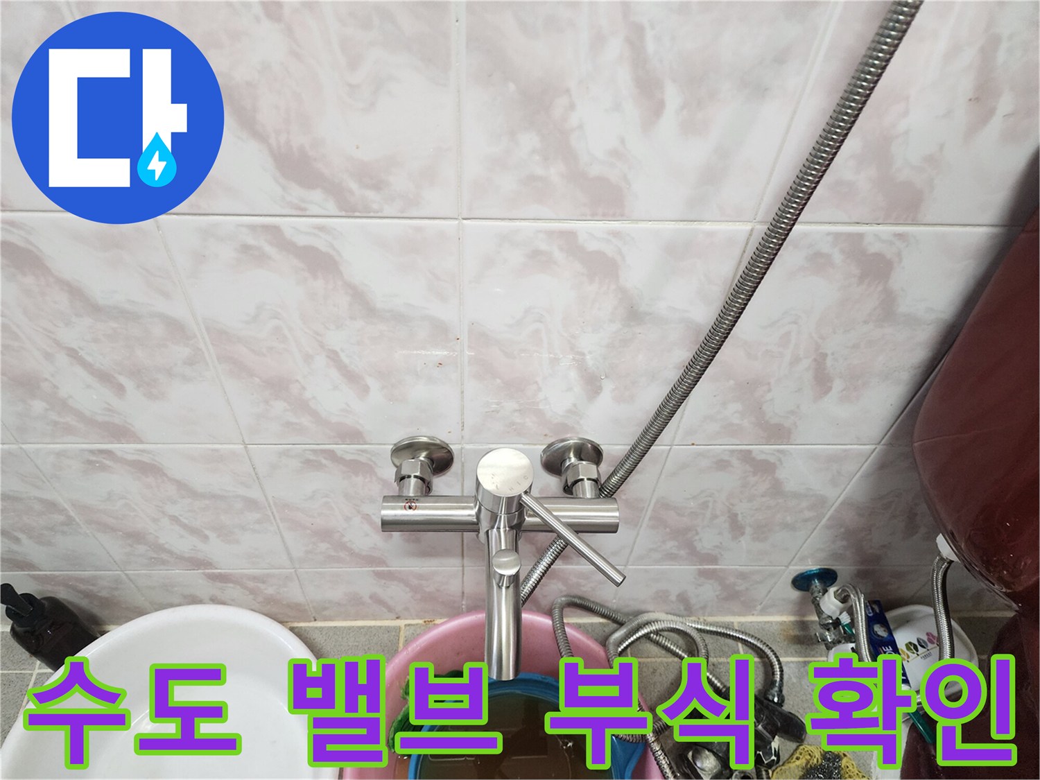 타일 벽면에 설치된 금속 재질의 수도 밸브와 연결 호스 모습입니다.