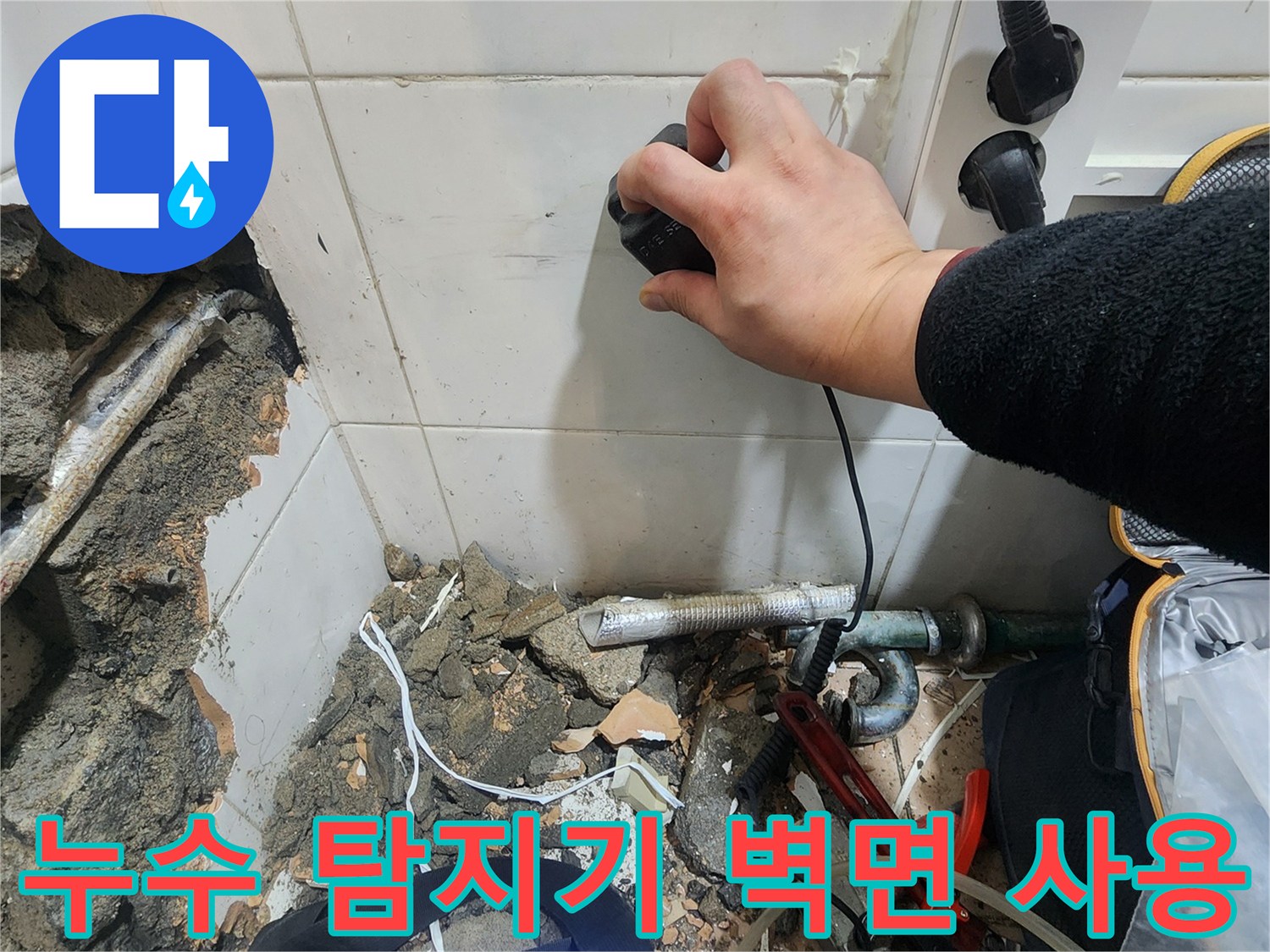 벽면 타일 부근에서 누수 지점을 찾기 위해 장비를 움직이는 손