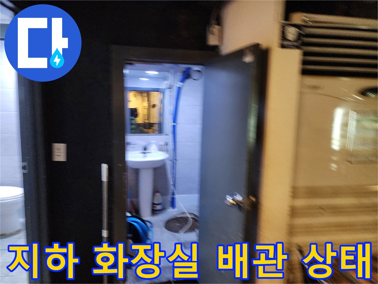 지하층 화장실 내부의 노출된 파란색 주름관과 세면대 하부 배관 모습입니다.
