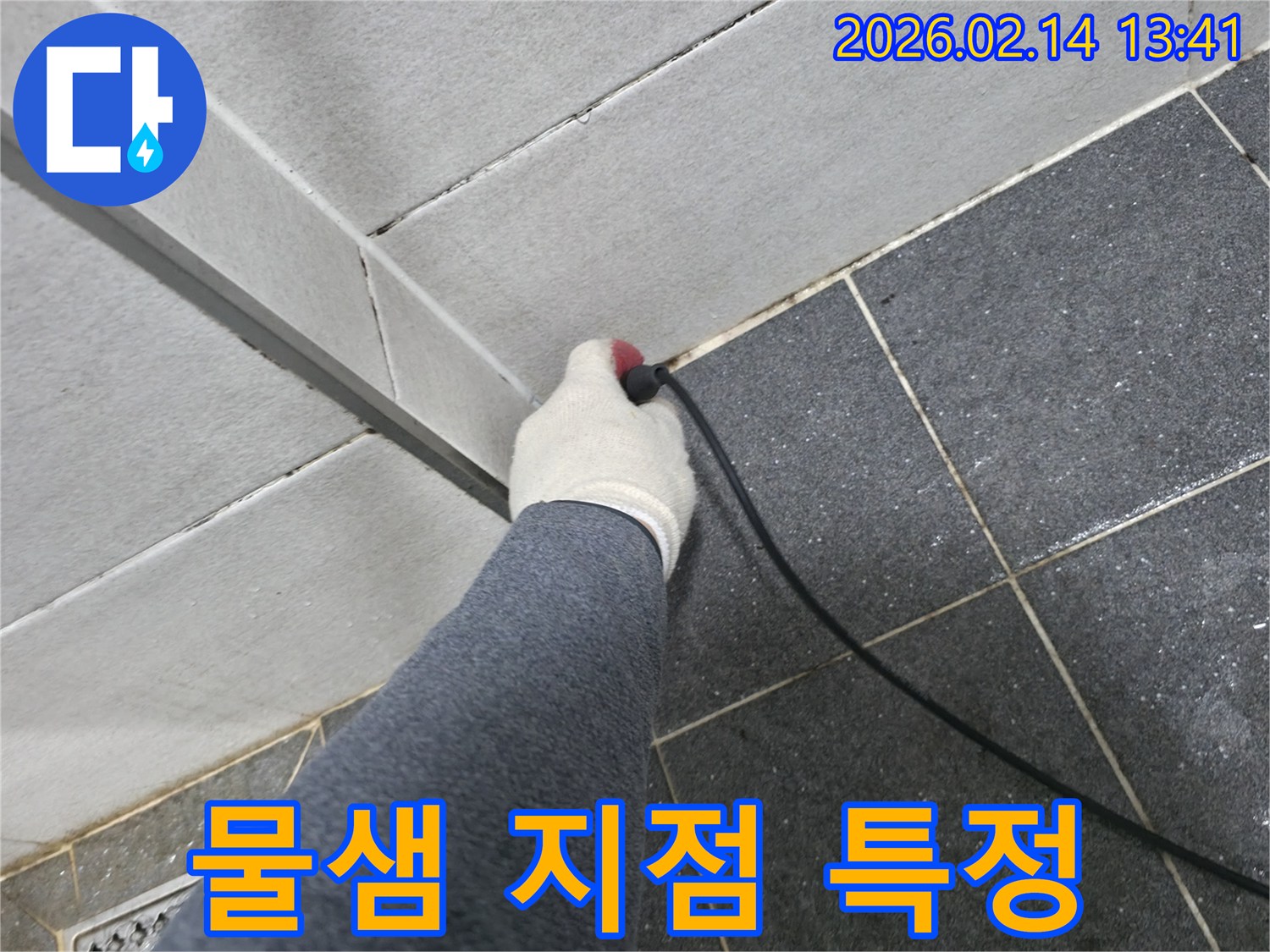 누수 엔지니어가-작업 장갑을 끼고-누수 탐지 장비로-타일 틈새에서-물이 새는 지점을-정확히 특정하는 장면입니다.