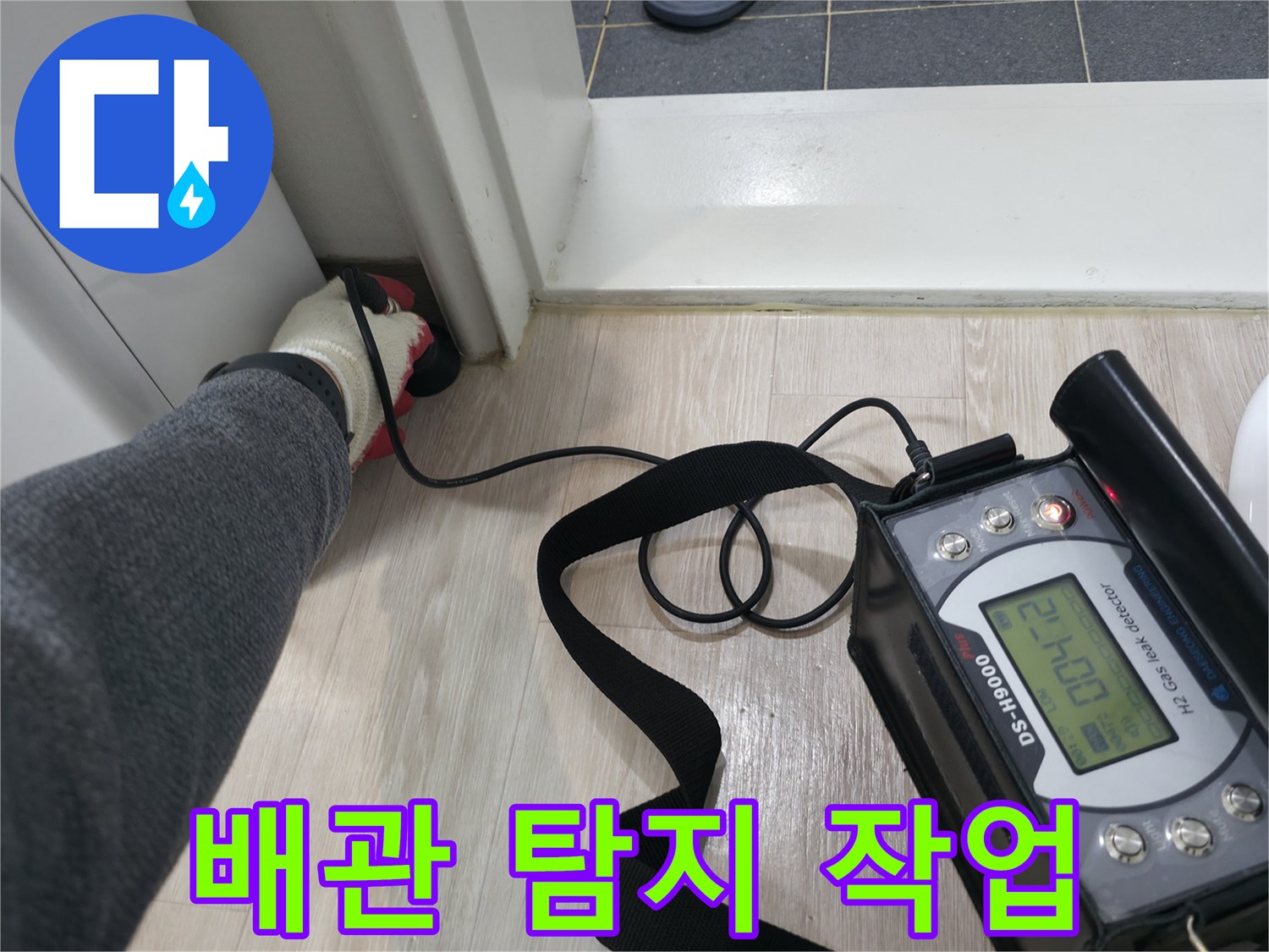 바닥 타일 근처에서-청음식 장비로-배관의 물샘 소리를 찾는 장면