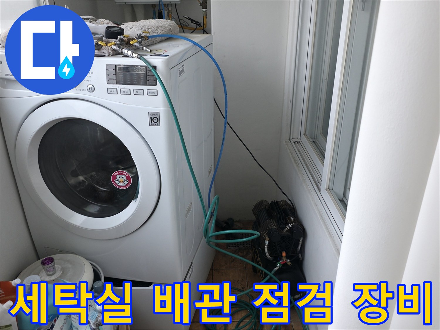 세탁기 주변의 수도 연결 부위와 압력 테스트를 위한 호스가 연결된 모습입니다.