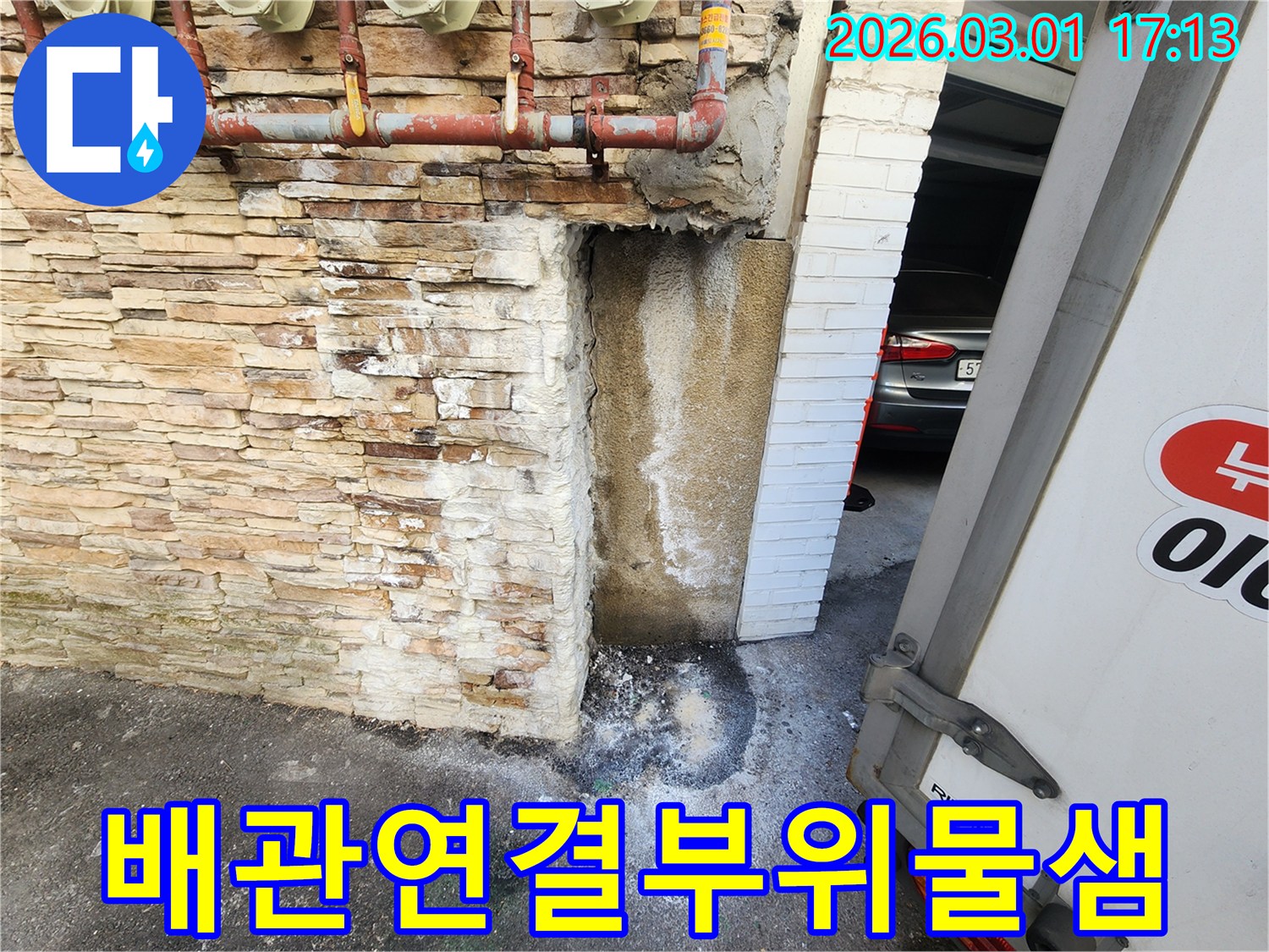 건물 외벽에 설치된-배관의 연결부위에서-물이 새어 나와-벽면이 젖고-바닥에 물이 고인-누수 현장
