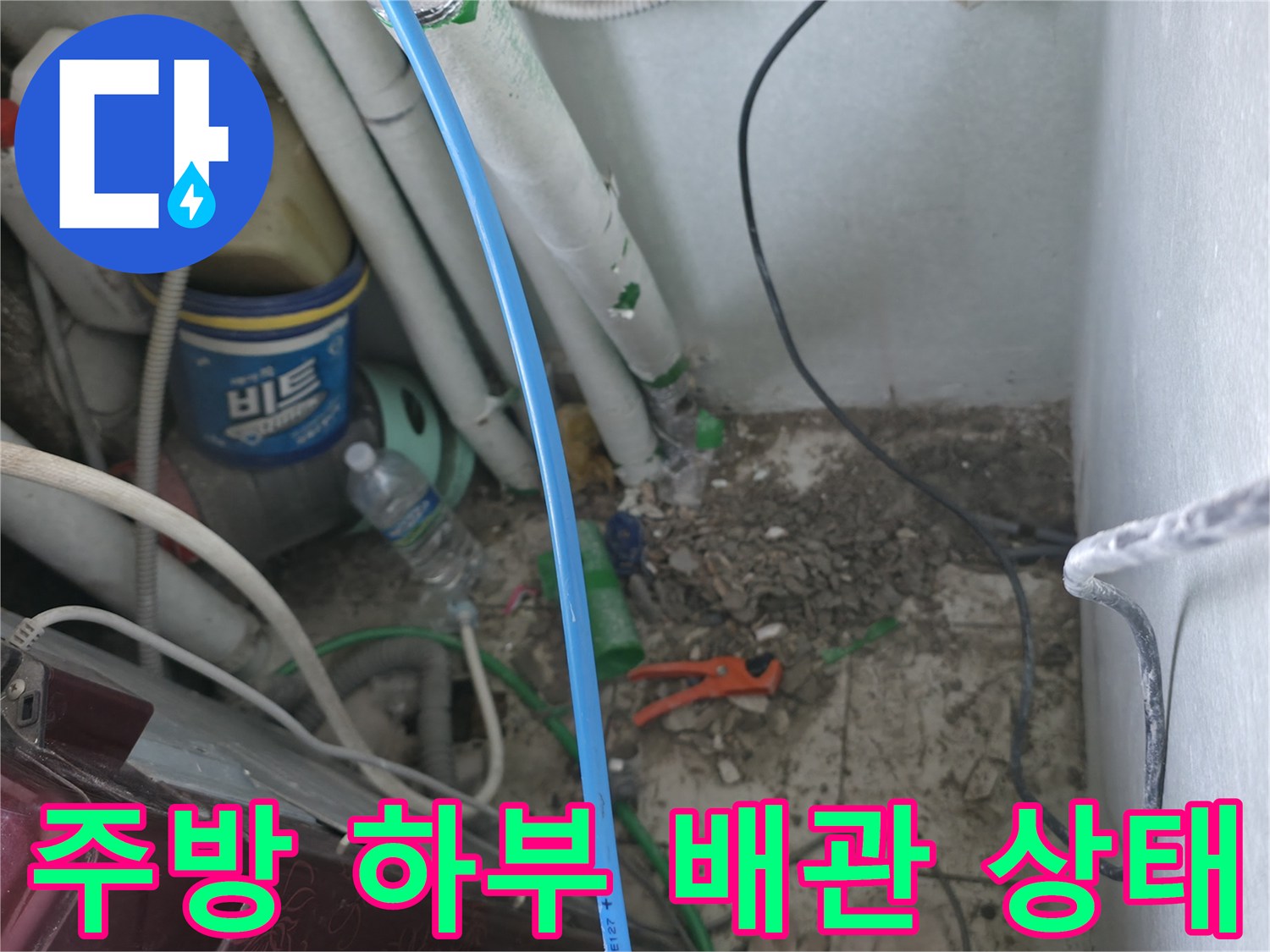 싱크대 아래쪽 복잡한 배관 및 주변 자재들이 놓여 있는 모습입니다.