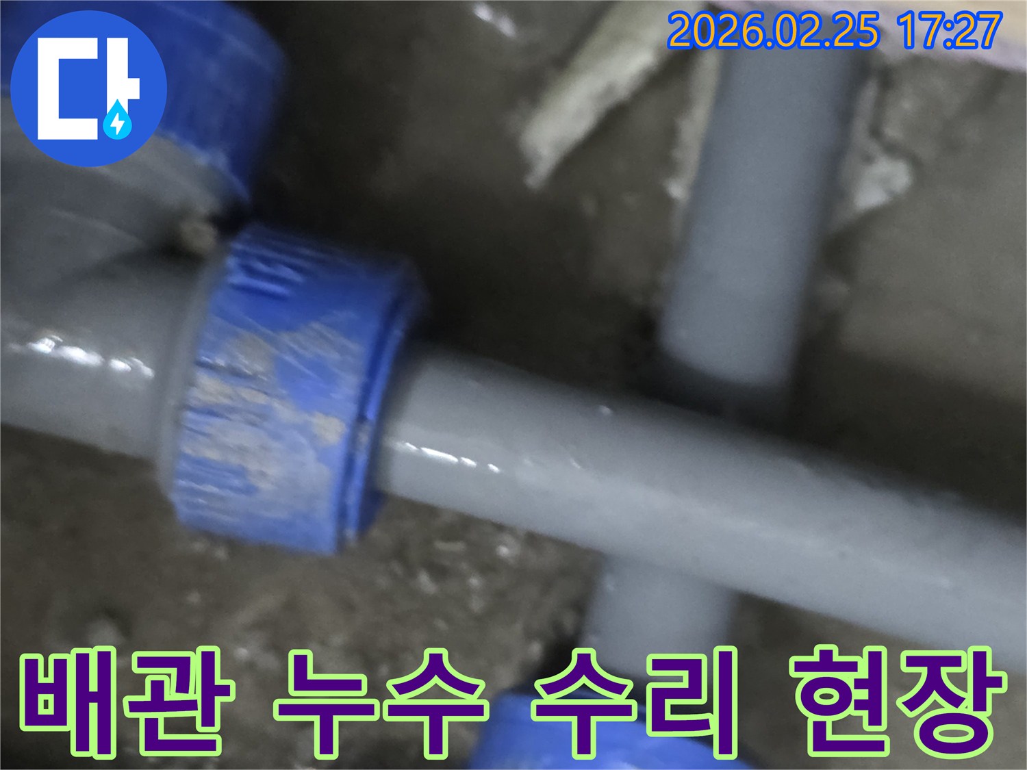 이 이미지는 주택 내부에서 발생한 배관 누수-수리 현장을 보여주며-회색 파이프와 파란색 연결 부품이 특징입니다.