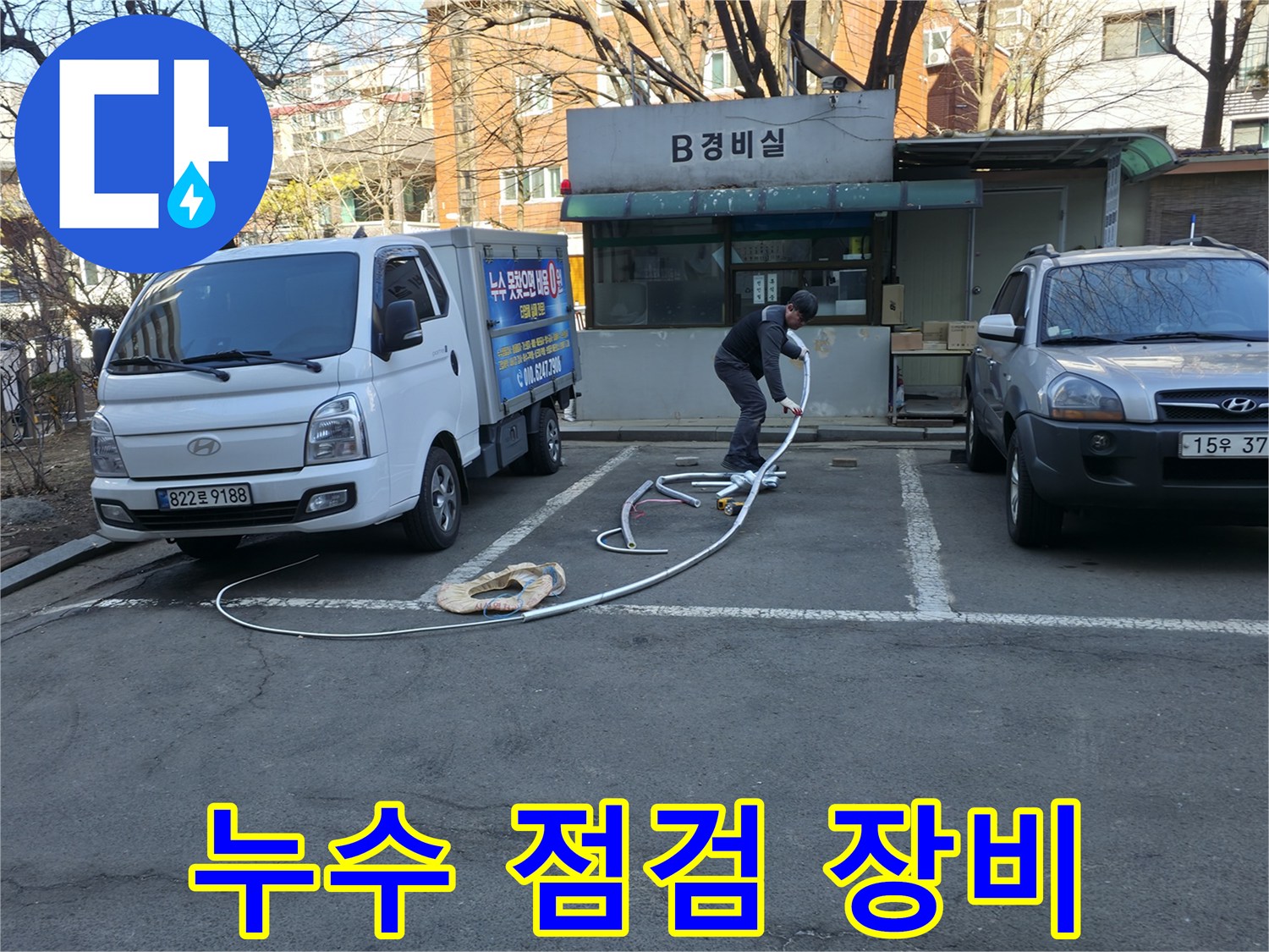 경비실 앞 작업 차량과 바닥에 연결된 흰색 호스