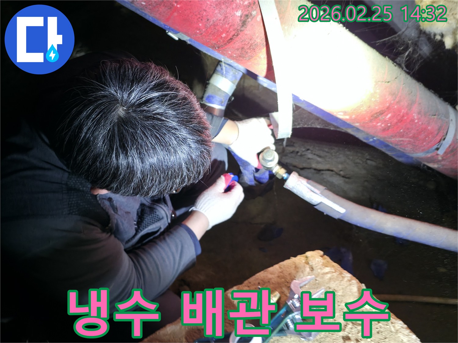 숙련된 누수 기술자가 좁은 공간에서 손전등을 비추며 냉수 배관 연결 부위를 정밀하게 점검하고 보수하고 있습니다-냉수누수해결-전문가보수