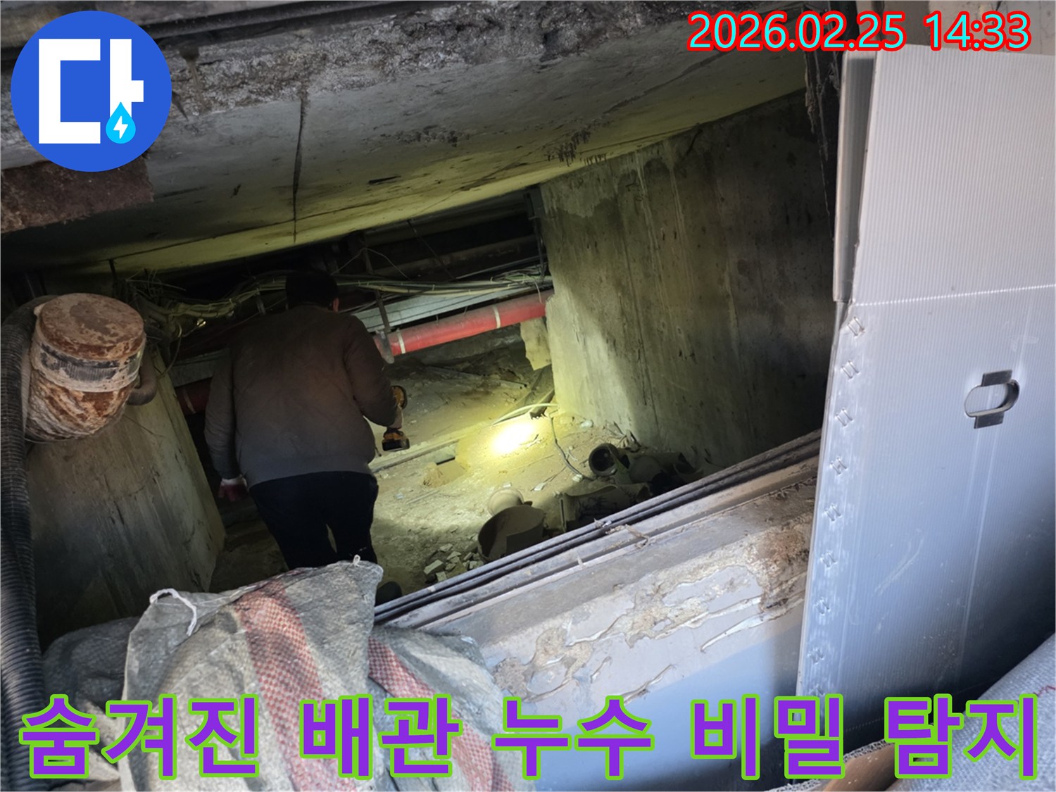 숙련된 누수 전문 엔지니어가-어둡고 협소한 공간에서-손전등을 비추며-숨겨진 배관의 미세한 누수 원인을-정밀하게 탐색하는 모습입니다.