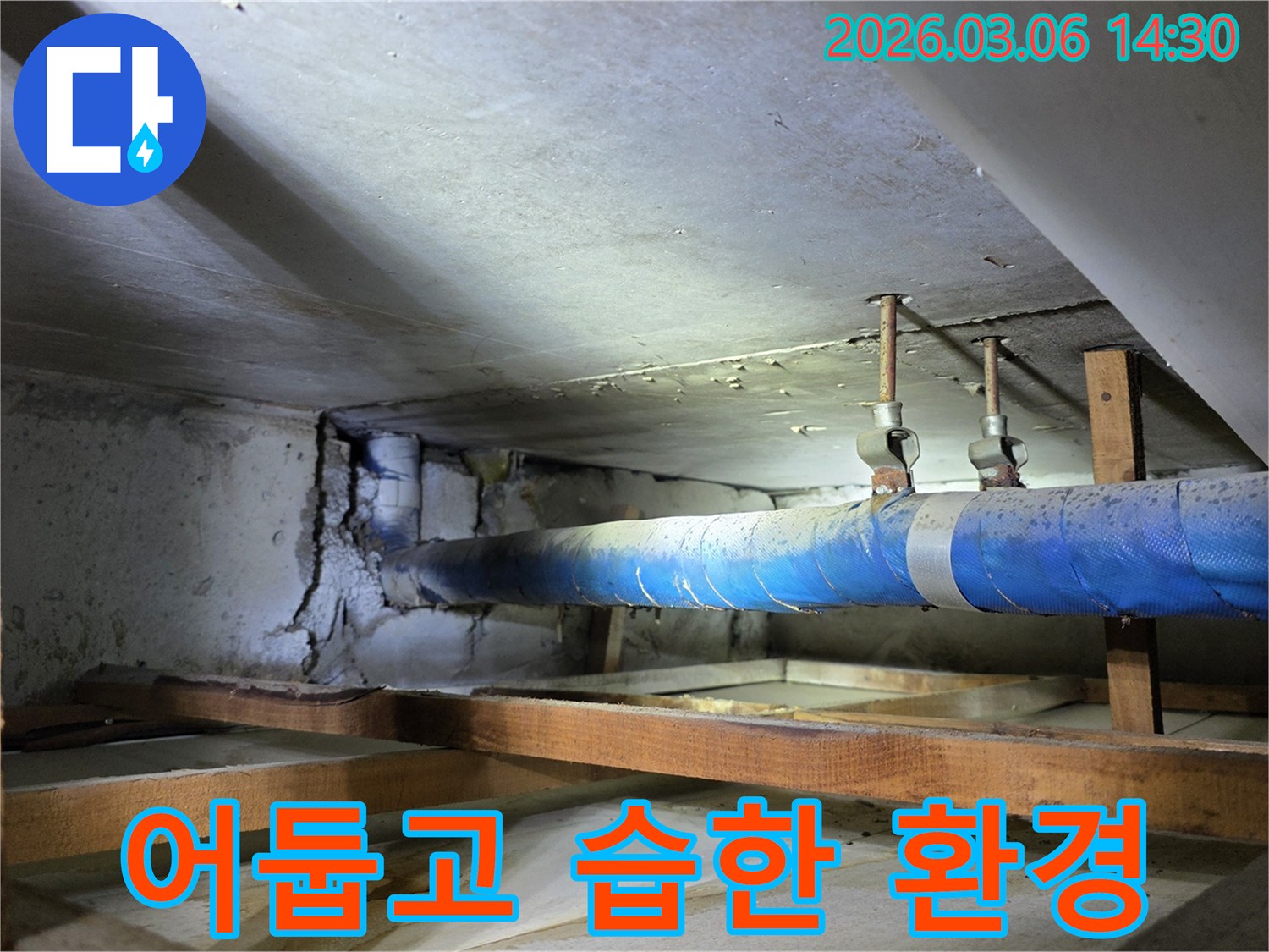 지하 공간의 파란색 배관 주변-어둡고 습한 환경에서-누수로 인해 손상된 콘크리트 벽면을-누수 엔지니어가-환경 개선을 위해-점검하는 모습