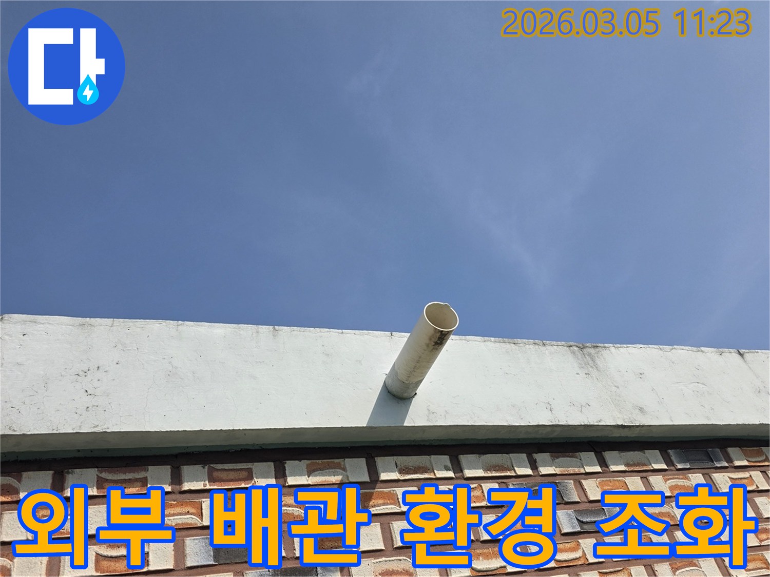 맑고-푸른-하늘-아래-건물-외벽에서-돌출된-배수관이-주변-환경과-어우러진-모습을-담은-사진입니다.