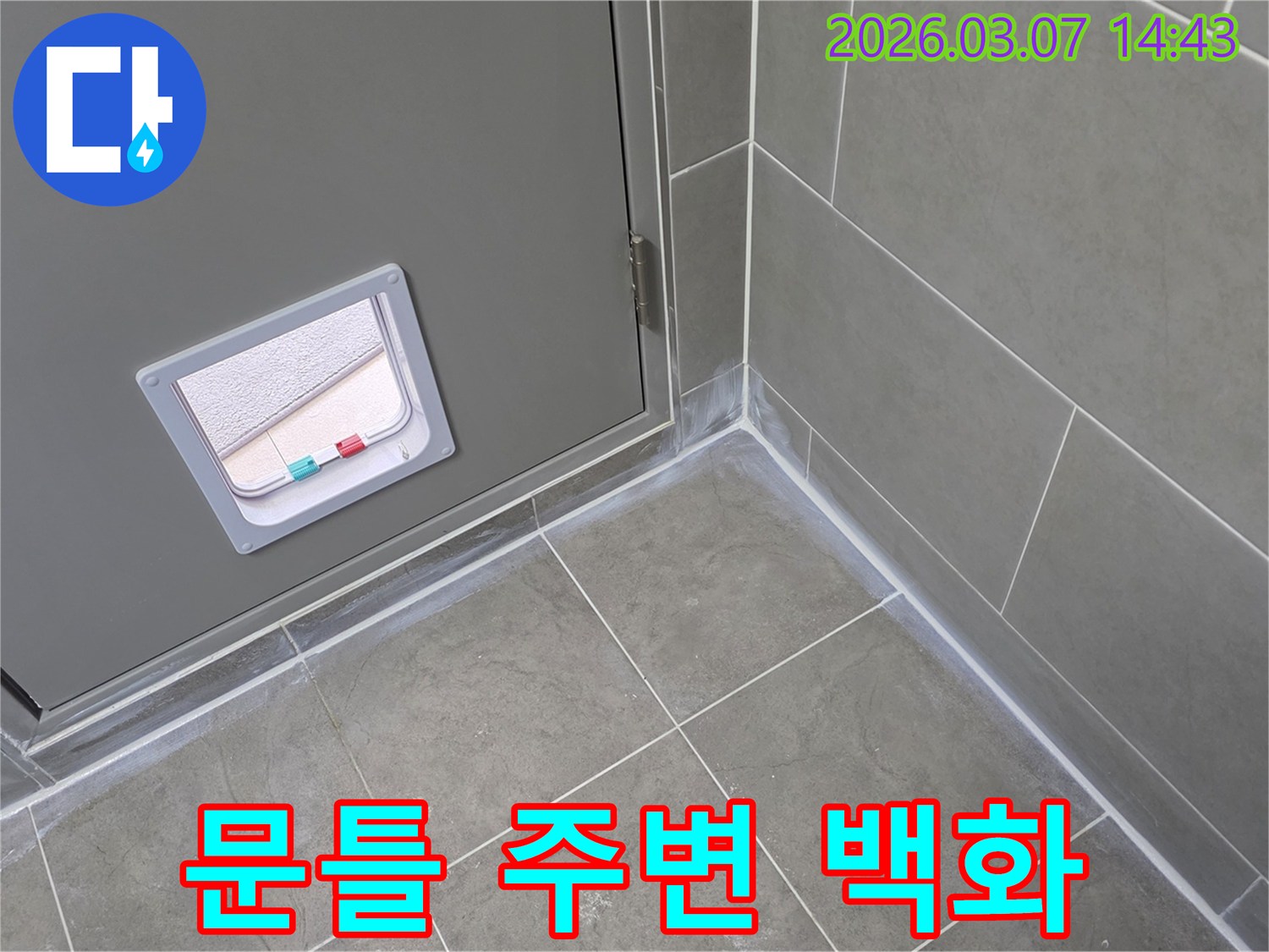 이 사진은 회색 문틀 하단과 인접한 타일 바닥-그리고 벽면에 발생한 백화 현상을 통해-누수 문제를 시각적으로 보여줍니다.