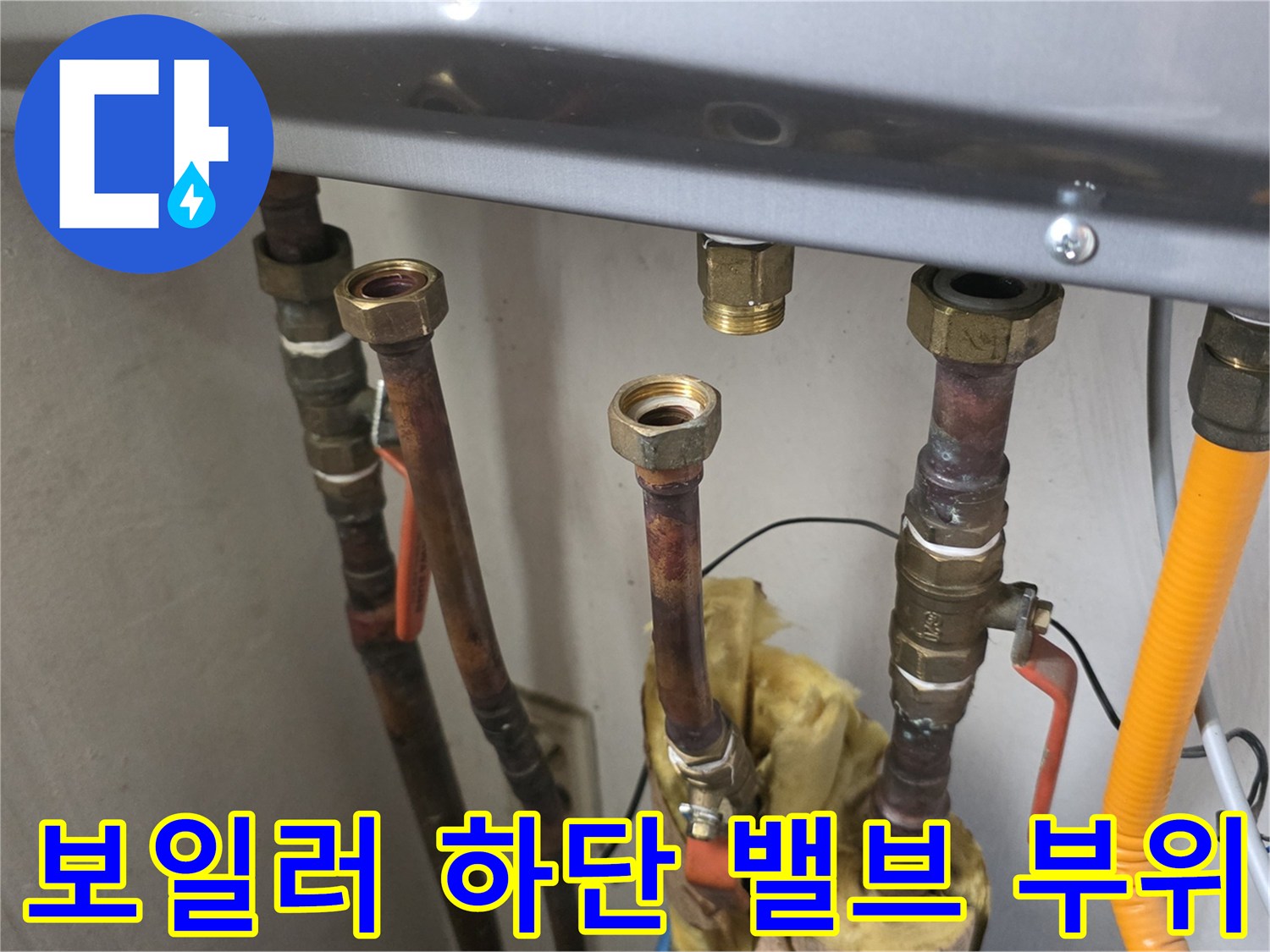 보일러 본체 아래 설치된 다양한 크기의 배관과 노란색 호스 모습입니다.