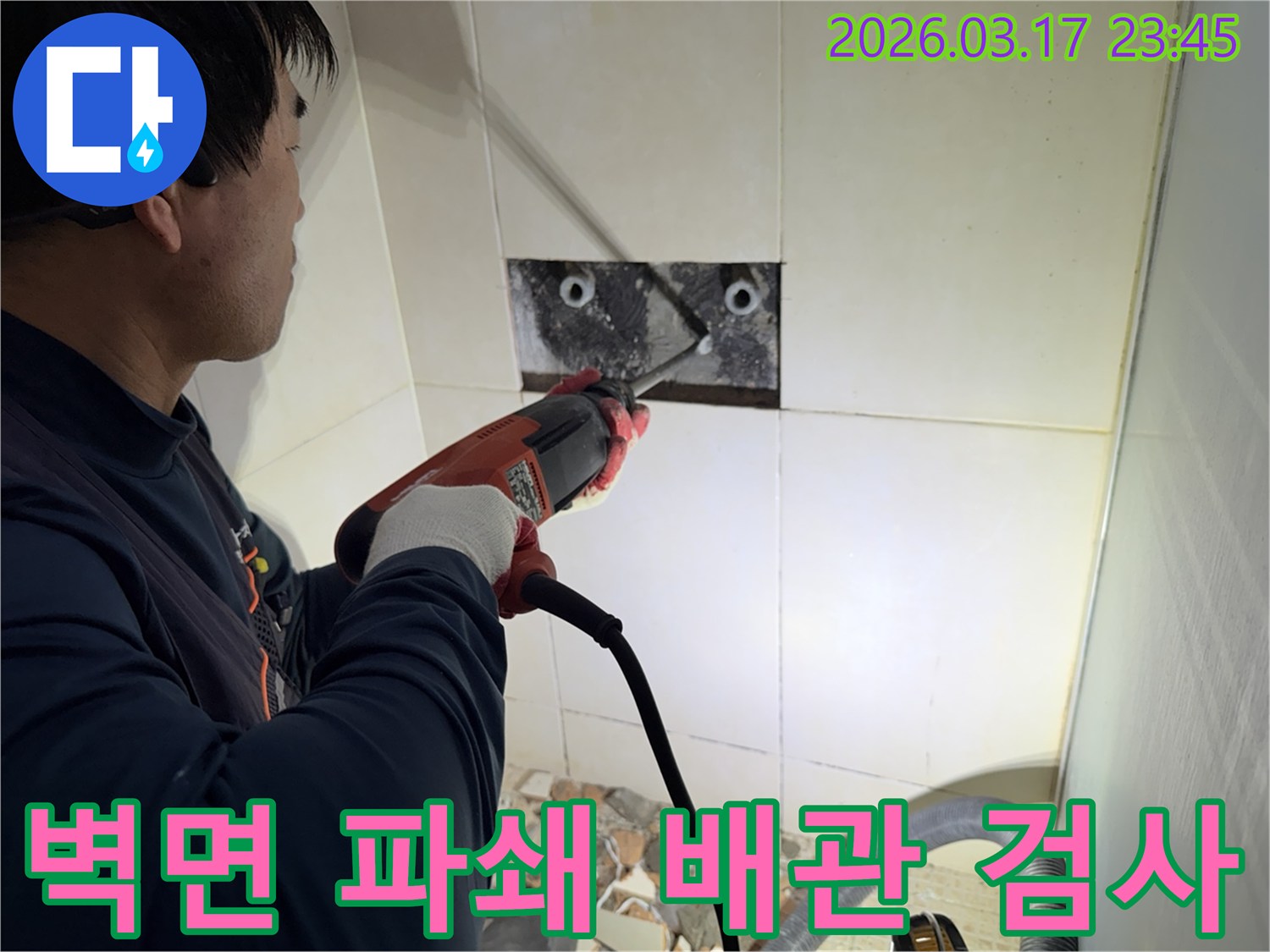 누수 공사 전문가가 주택 욕실 벽면의 타일을 조심스럽게 파쇄하여-누수 원인을 찾기 위한 배관 육안 검사 작업을 진행하는 모습입니다.