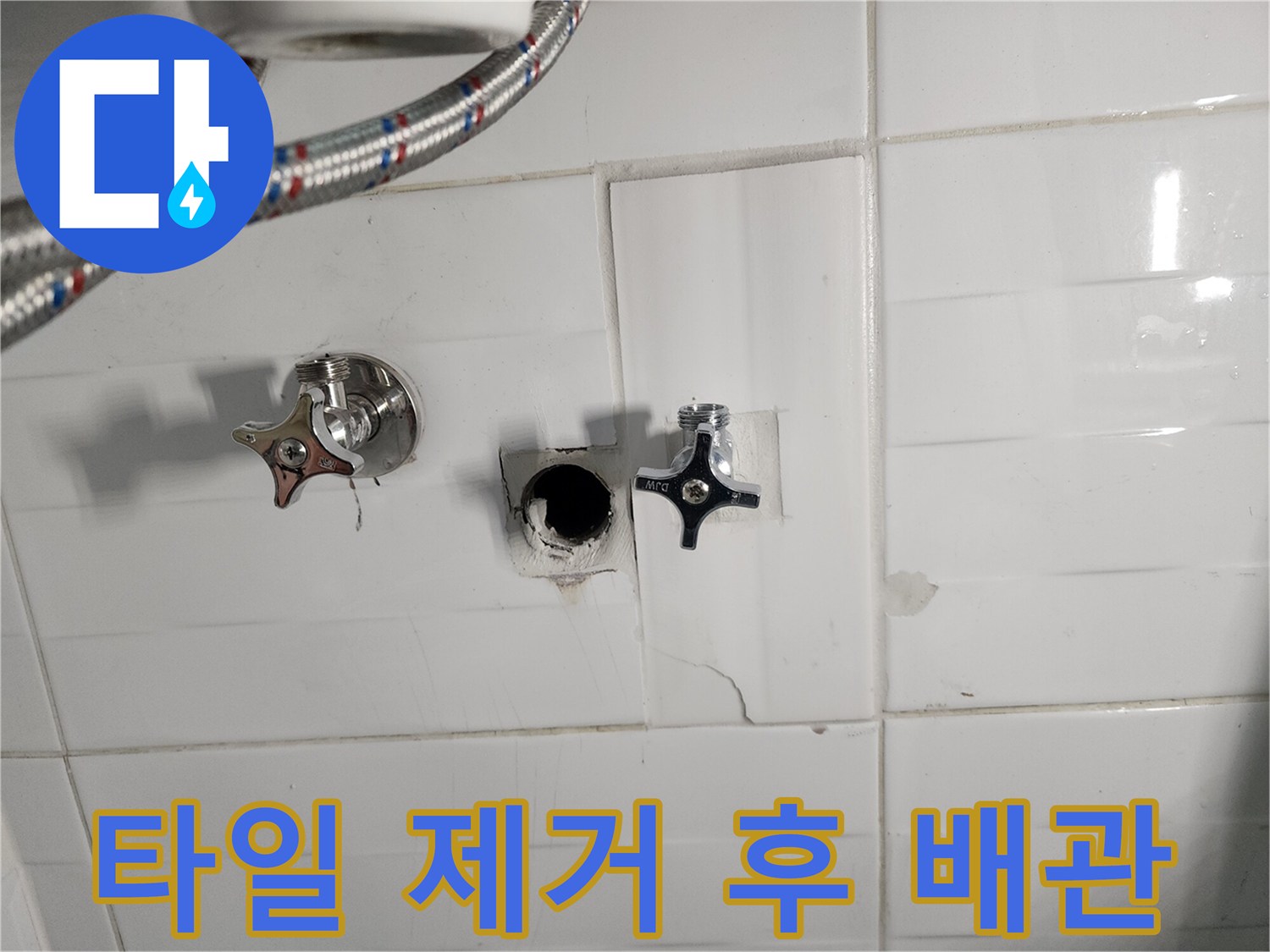 화장실 타일 내부의 노출된 수도 밸브와 연결된 금속 호스