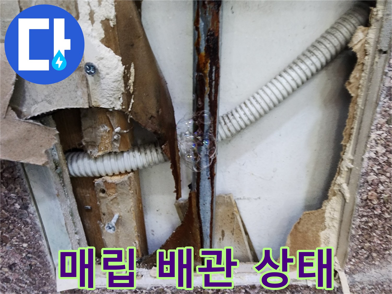 타공된 벽 안쪽의 녹슨 금속 관과 하얀색 주름 호스 모습
