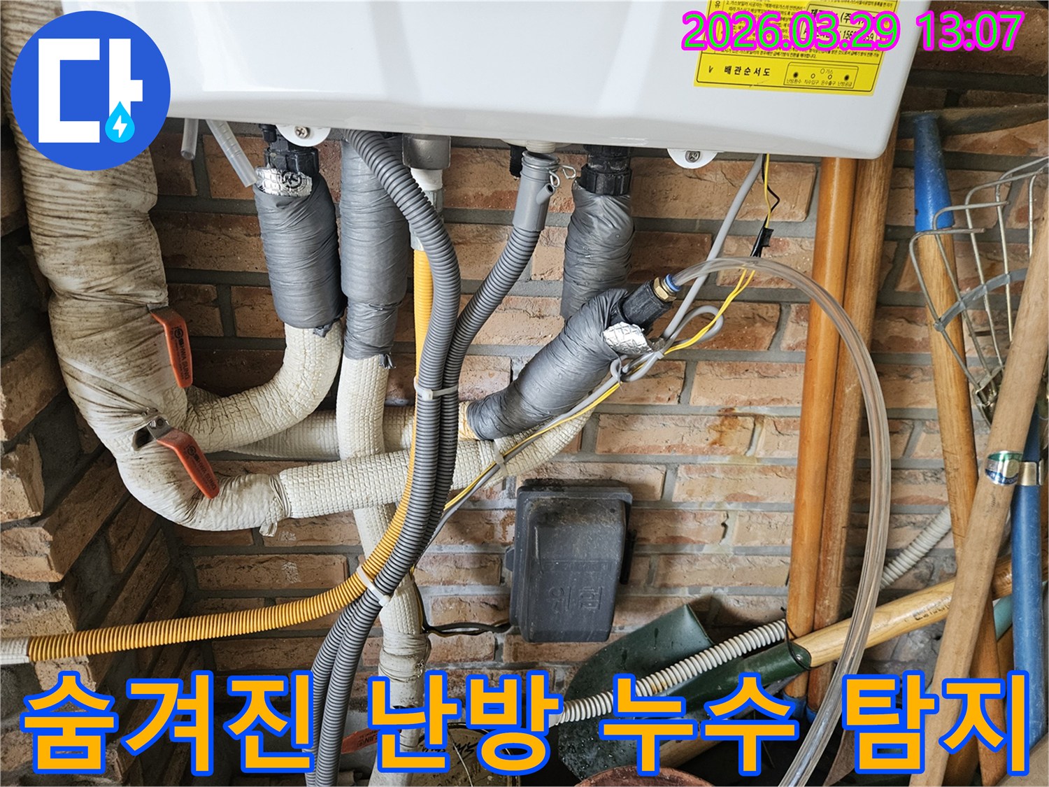 벽돌 벽을 배경으로 회색 단열재로 감싸진 난방 배관들이-숨겨진 누수 지점을 찾기 위해-정밀하게 탐지되고 있습니다.