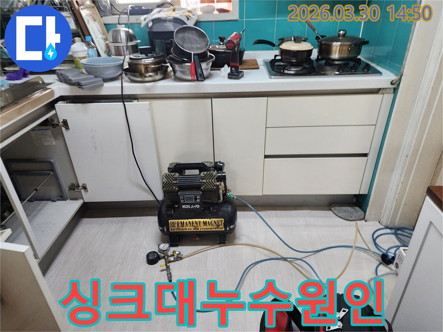 싱크대 하부장 안쪽에-누수 탐지를 위한 공압 장비가 설치되어-배관 압력 검사를 진행하고 있습니다.