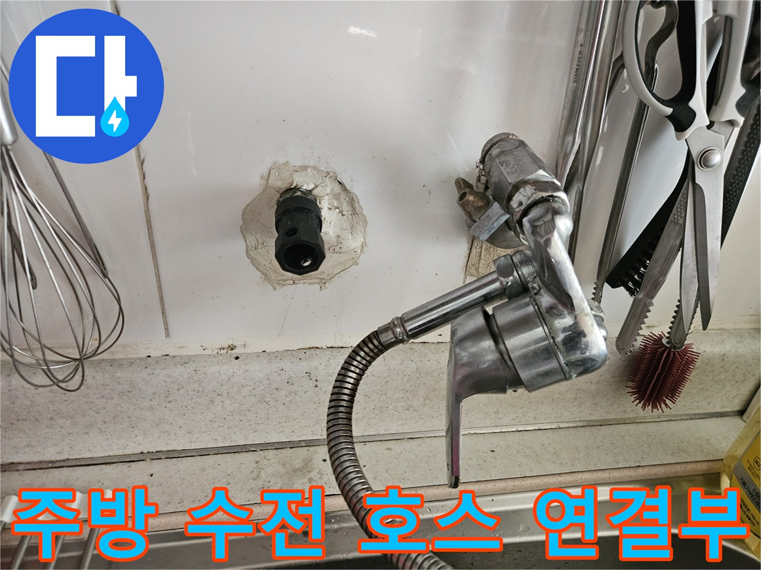 벽면에 노출된 검은색 배관 입구와 금속 재질의 유연한 수전 호스