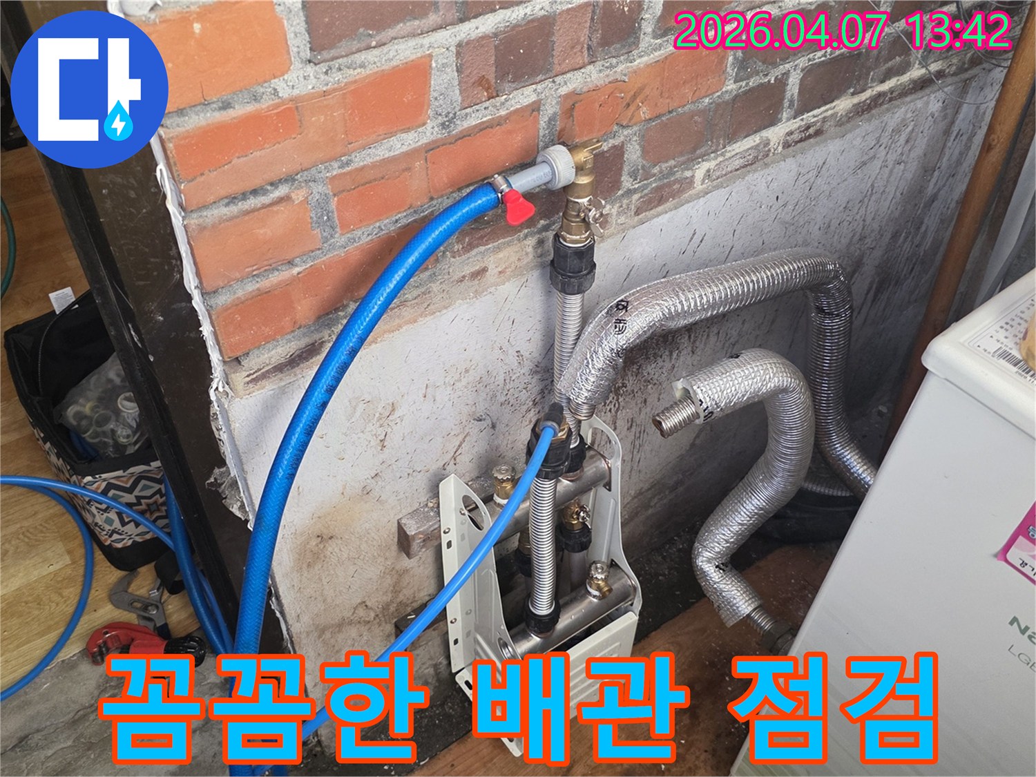 벽돌 벽 옆에-누수 탐지 장비와-다양한 배관들이 놓여 있으며-전문가가 꼼꼼하게-배관 상태를 점검하는-모습을 담고 있습니다.