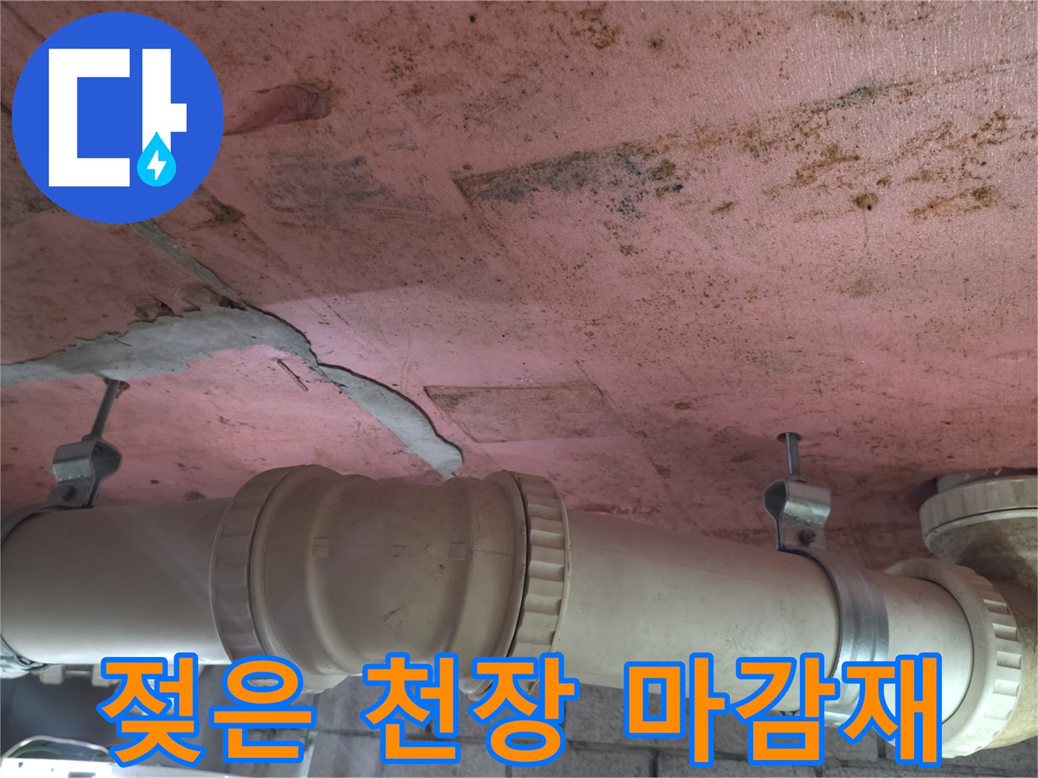 분홍색 천장 패널-배관 주변의 젖은 얼룩과 균열이 있는 모습입니다.