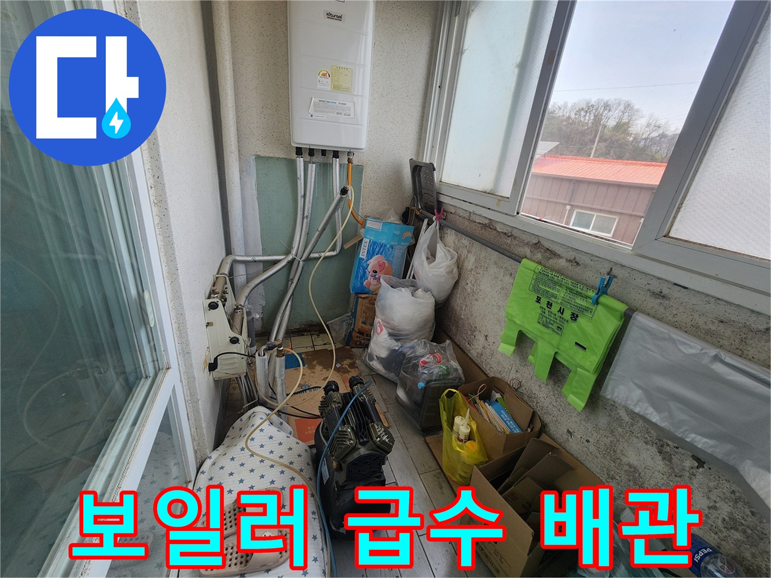 보일러 하단에 연결된 은색 배관과 주변 물건들이 놓인 베란다 모습