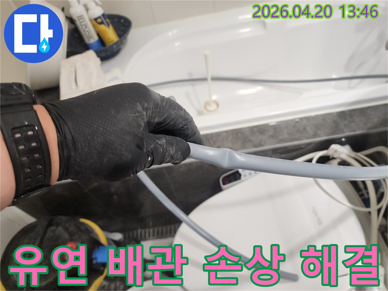검은 장갑을 낀 손이 욕실의 유연한 배관에 발생한-손상 부위를 확인하며 누수 해결을 위한-준비를 하고 있는 장면입니다.