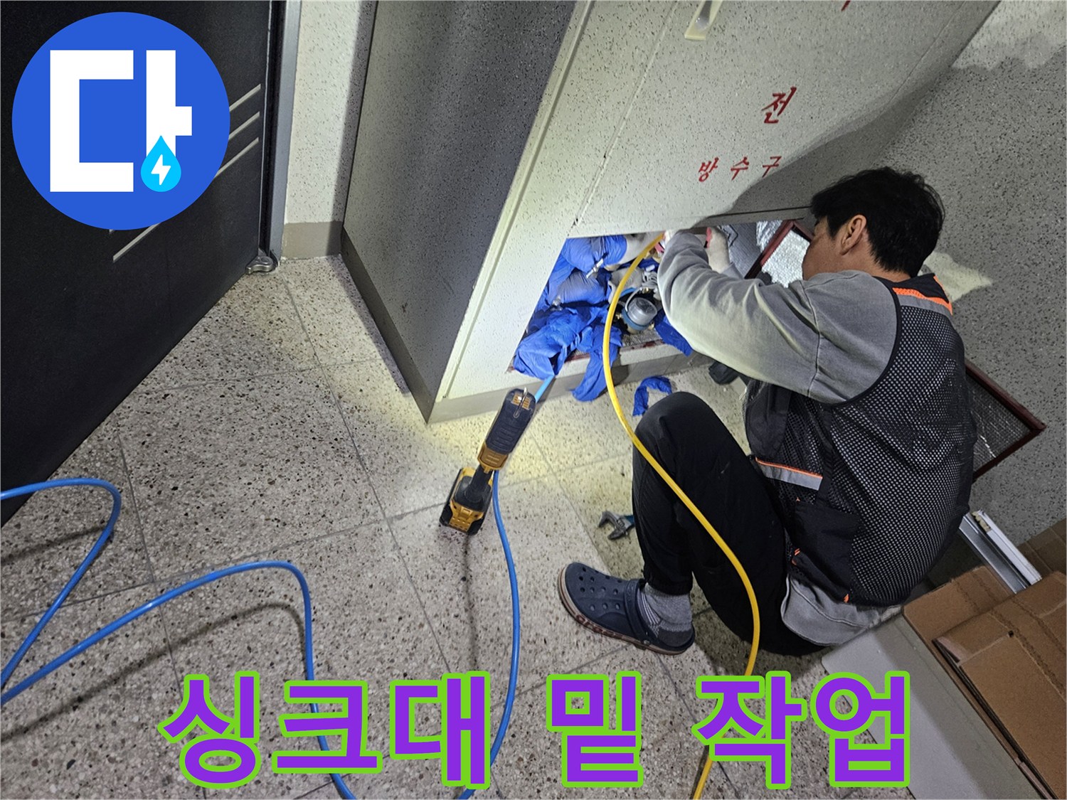 좁은 싱크대 하단 공간에서 배관 상태를 점검하며 도구를 사용하는 모습