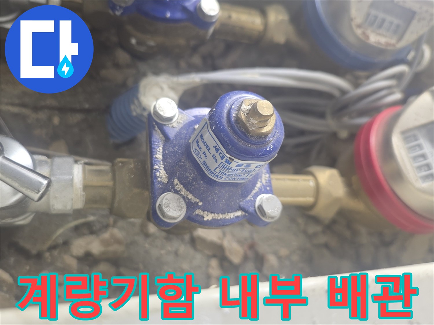 자갈로 채워진 계량기함 내부에 노출된 수도 배관과 밸브 모습입니다.