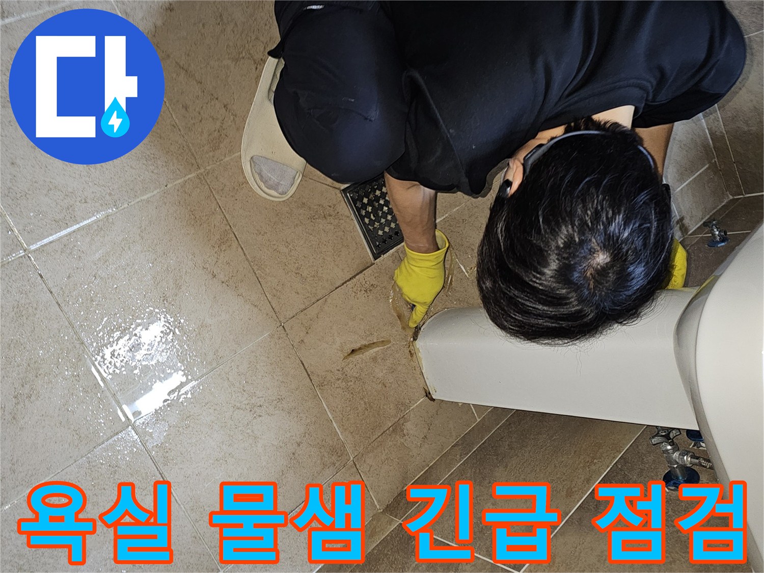 전문 엔지니어가-노란 장갑을 끼고-욕실 바닥의 젖은 타일과-세면대 하단부를-집중적으로 관찰하며-긴급 누수 지점을 파악하고 있습니다