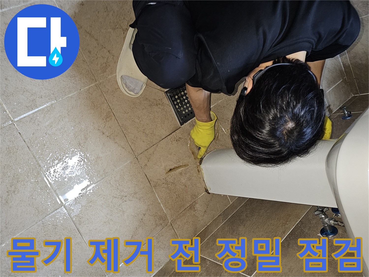 전문 엔지니어가-노란 장갑을 끼고-욕실 바닥의 젖은 타일과-세면대 하단부를-집중적으로 관찰하며-누수 지점을 파악하고 있습니다