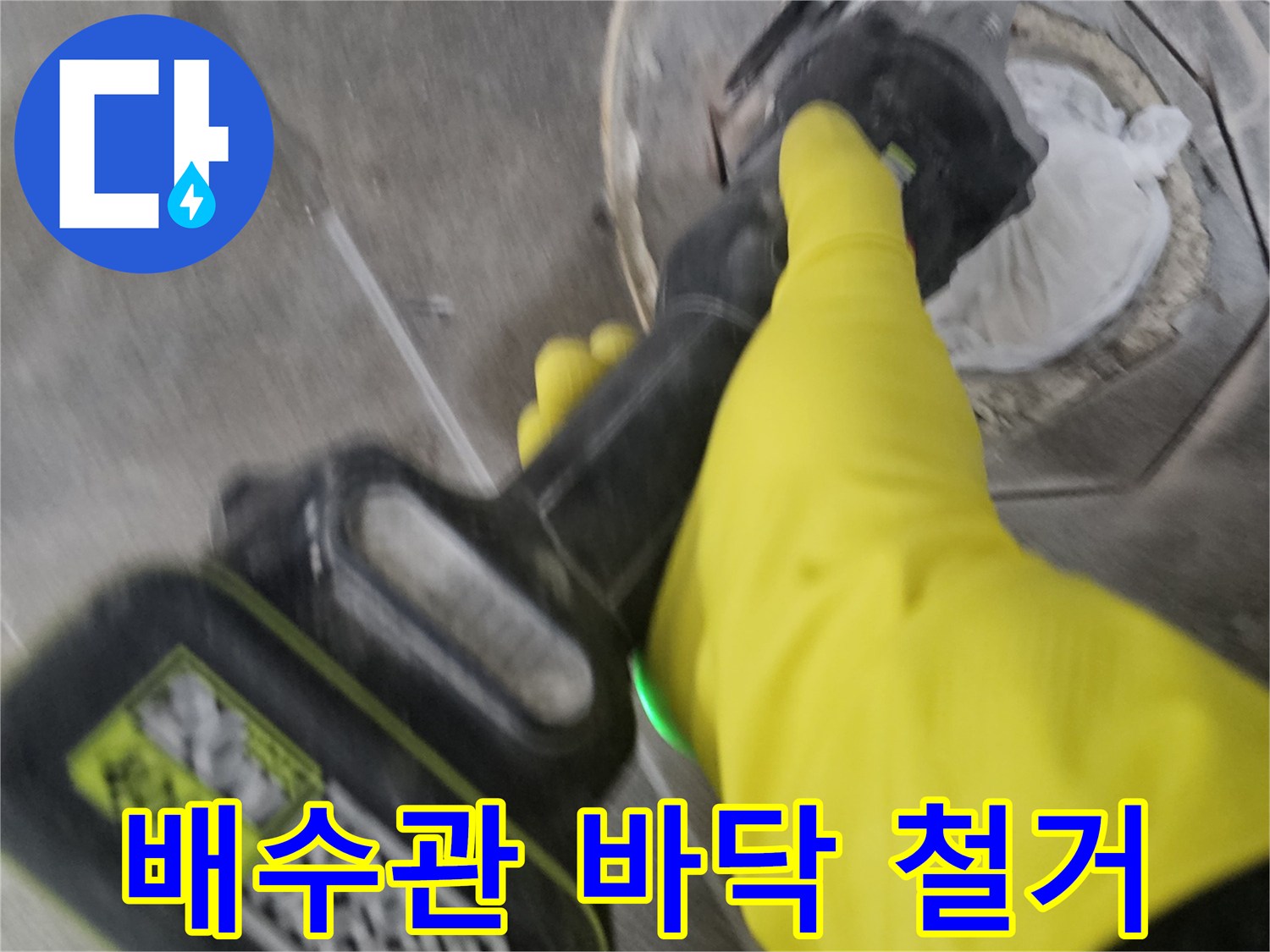 노란색 보호 장갑을 낀-전문가가-전동 절단기로-배수관 주변의 바닥 타일을-조심스럽게 철거하는 장면입니다.