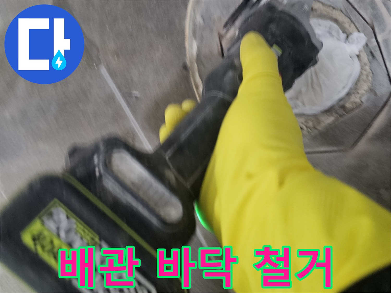 노란색 보호 장갑을 착용한-작업자가-전동 공구를 이용해-배관 주변의-굳은 타일을-조심스럽게 철거하는 모습입니다.