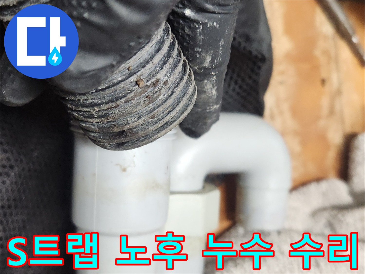 검은 장갑을 낀 손이-오랜 사용으로 노후된 S트랩 배관을-누수 방지를 위해 분리하고 있습니다