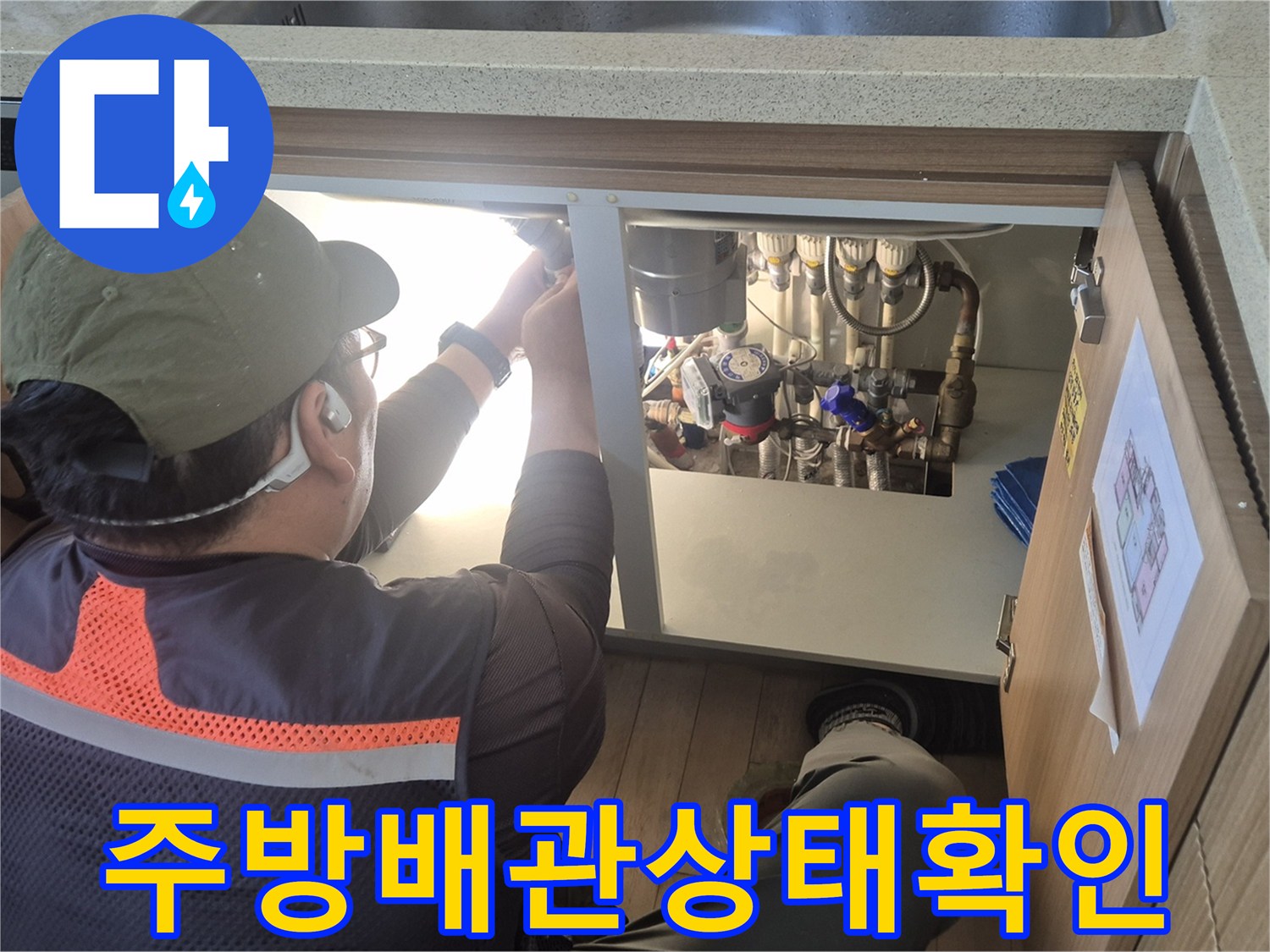 싱크대 아래쪽 좁은 공간에 설치된 배관들을 점검하는 작업자