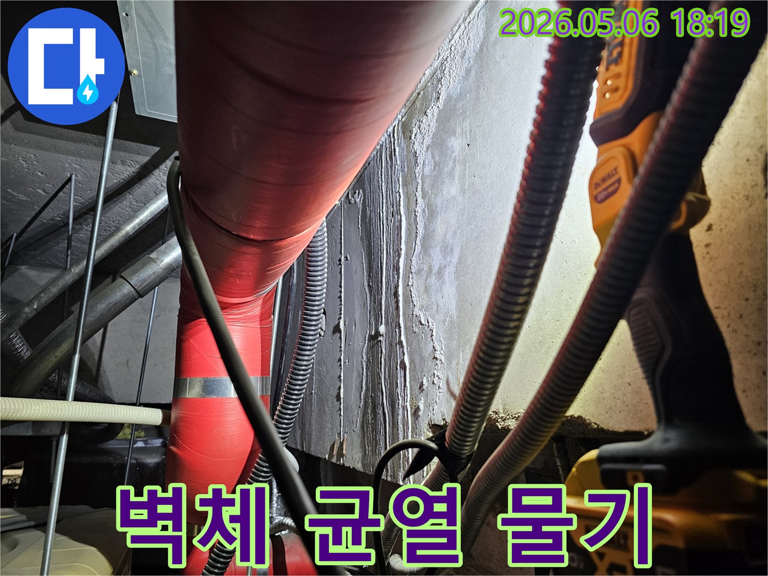 어두운 지하 공간에서-빨간색 배관 옆-콘크리트 벽면에-나타난-물기 침투-흔적과-잠재적인-균열을-조사하는-모습